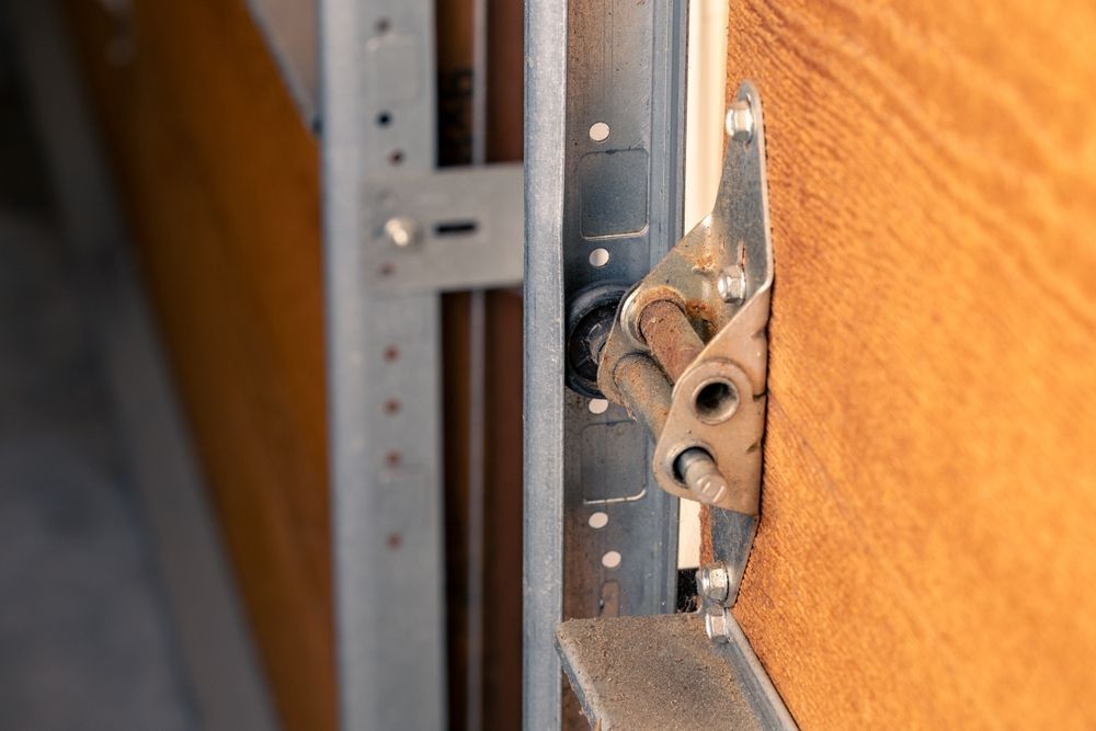 A close up of a garage door hinge on a wooden door.