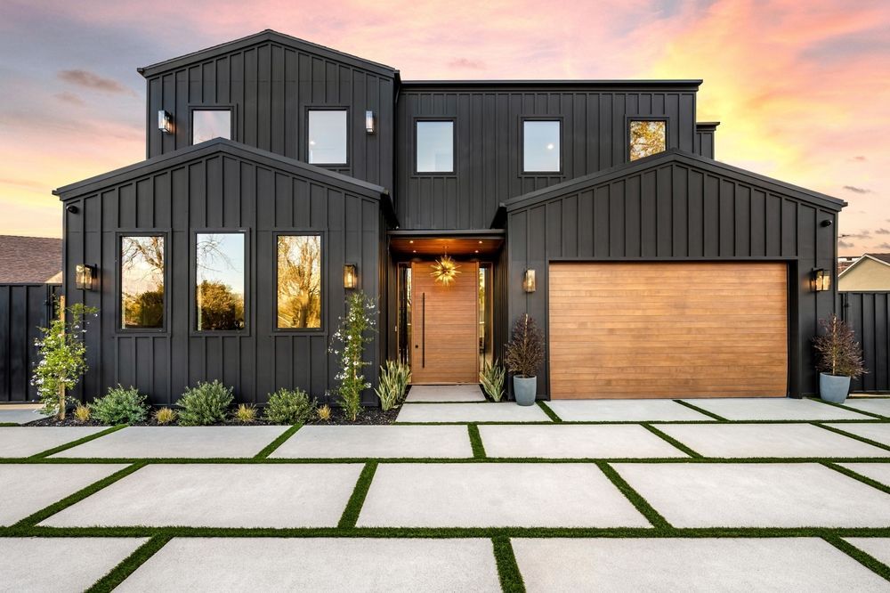 Modern black house with wooden garage door, rectangular concrete driveway, and grassy sections.