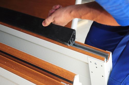 Person installing a black weather seal into a brown window frame.
