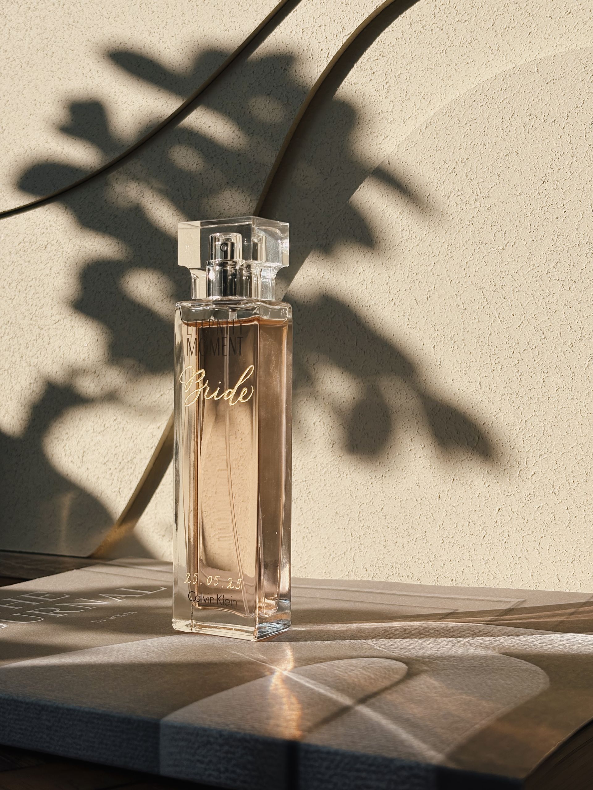 Een flesje parfum staat op een tafel voor een muur.