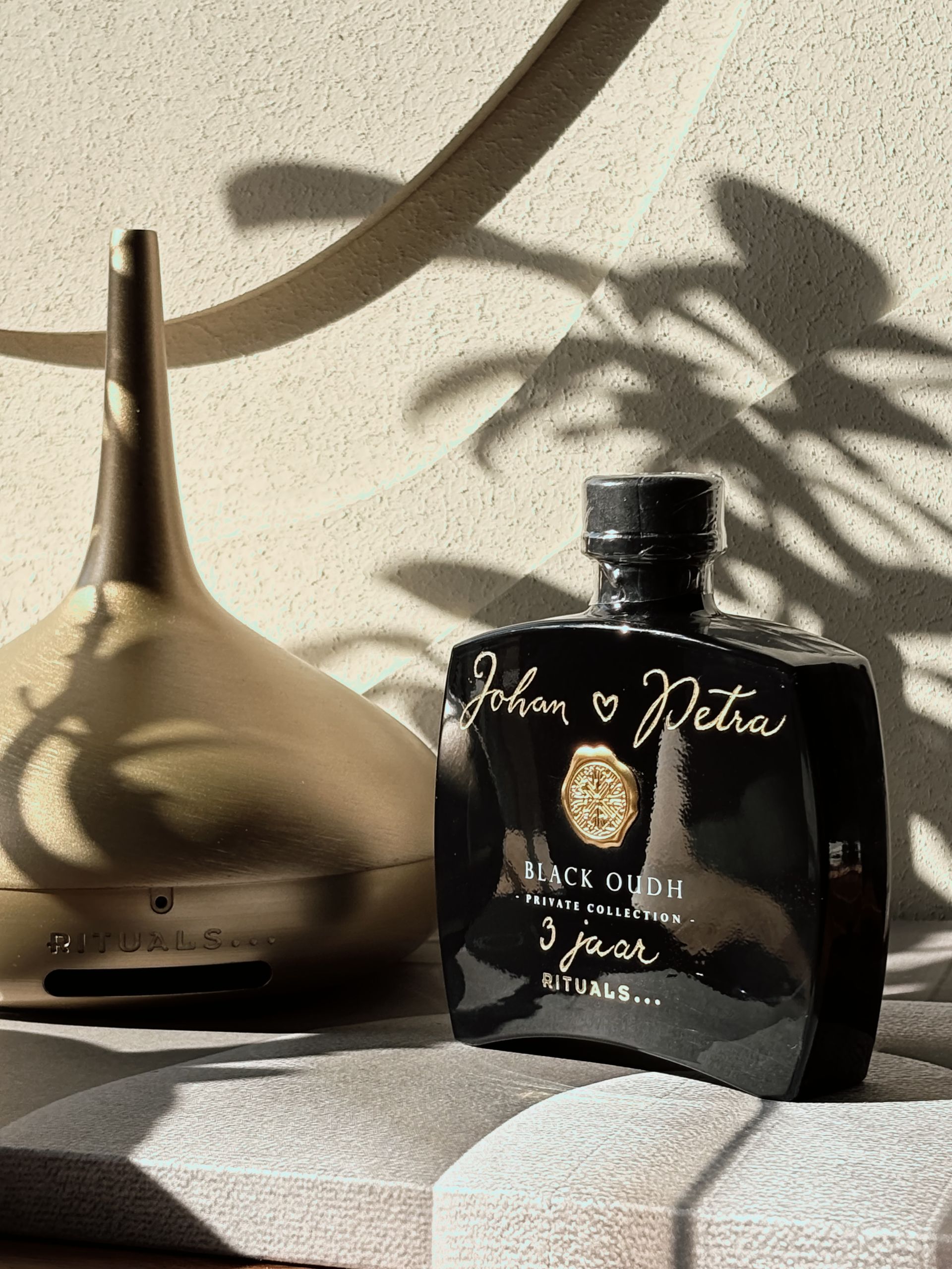 Een flesje parfum staat op een tafel naast een parfum genie van rituals.