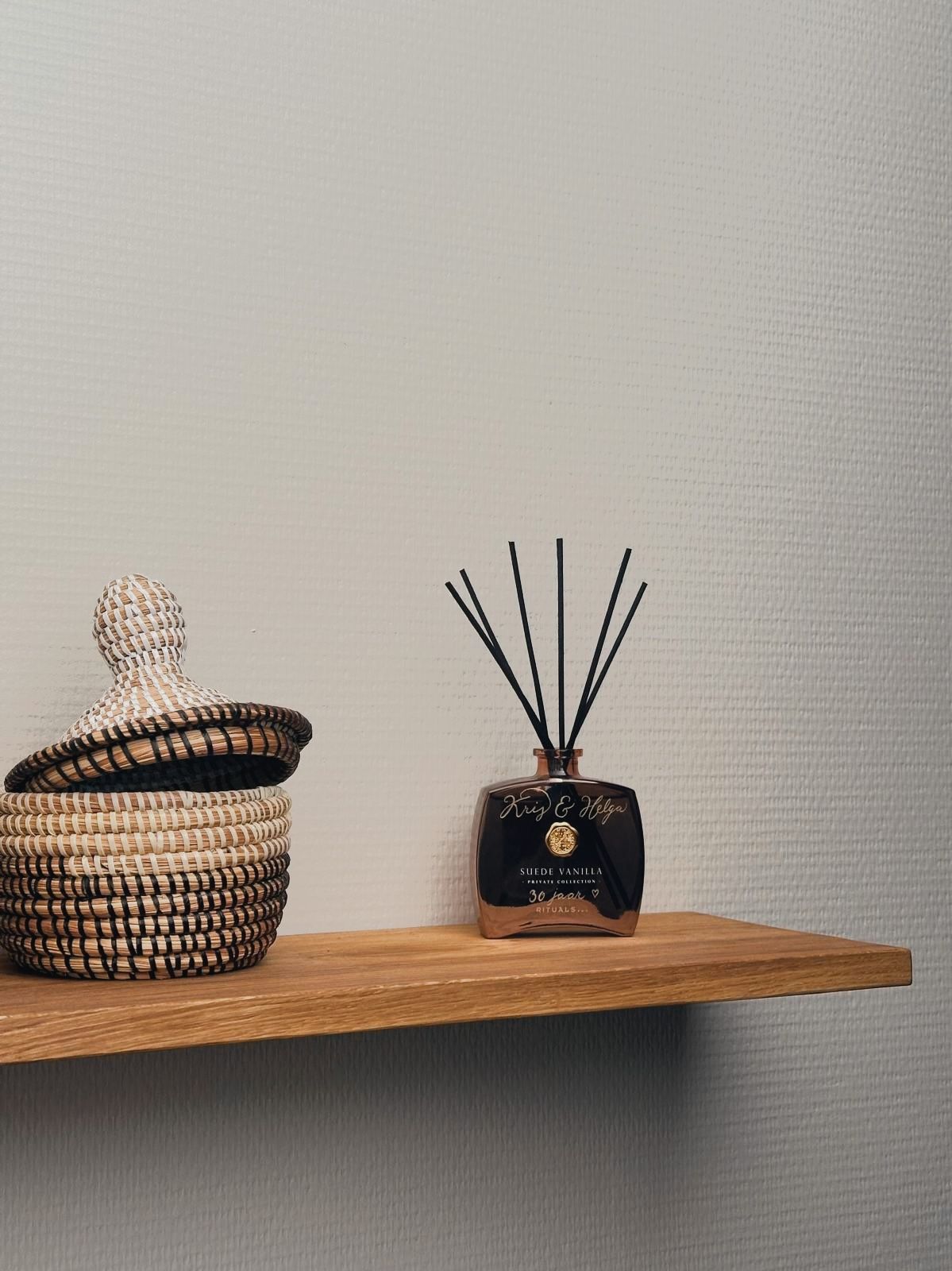 Een plank met daarop een mandje en een geurstokjesverspreider van Rituals.