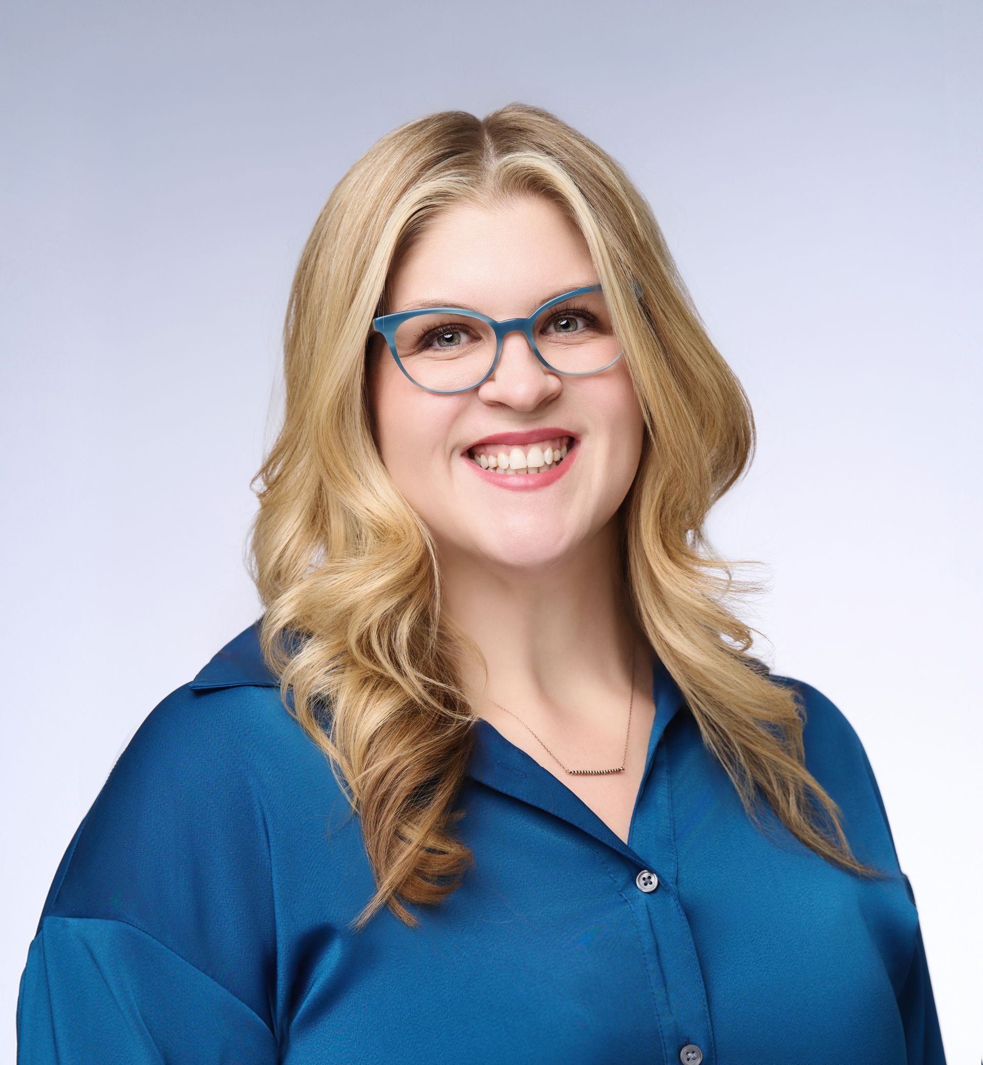 A woman wearing glasses and a blue shirt is smiling for the camera.