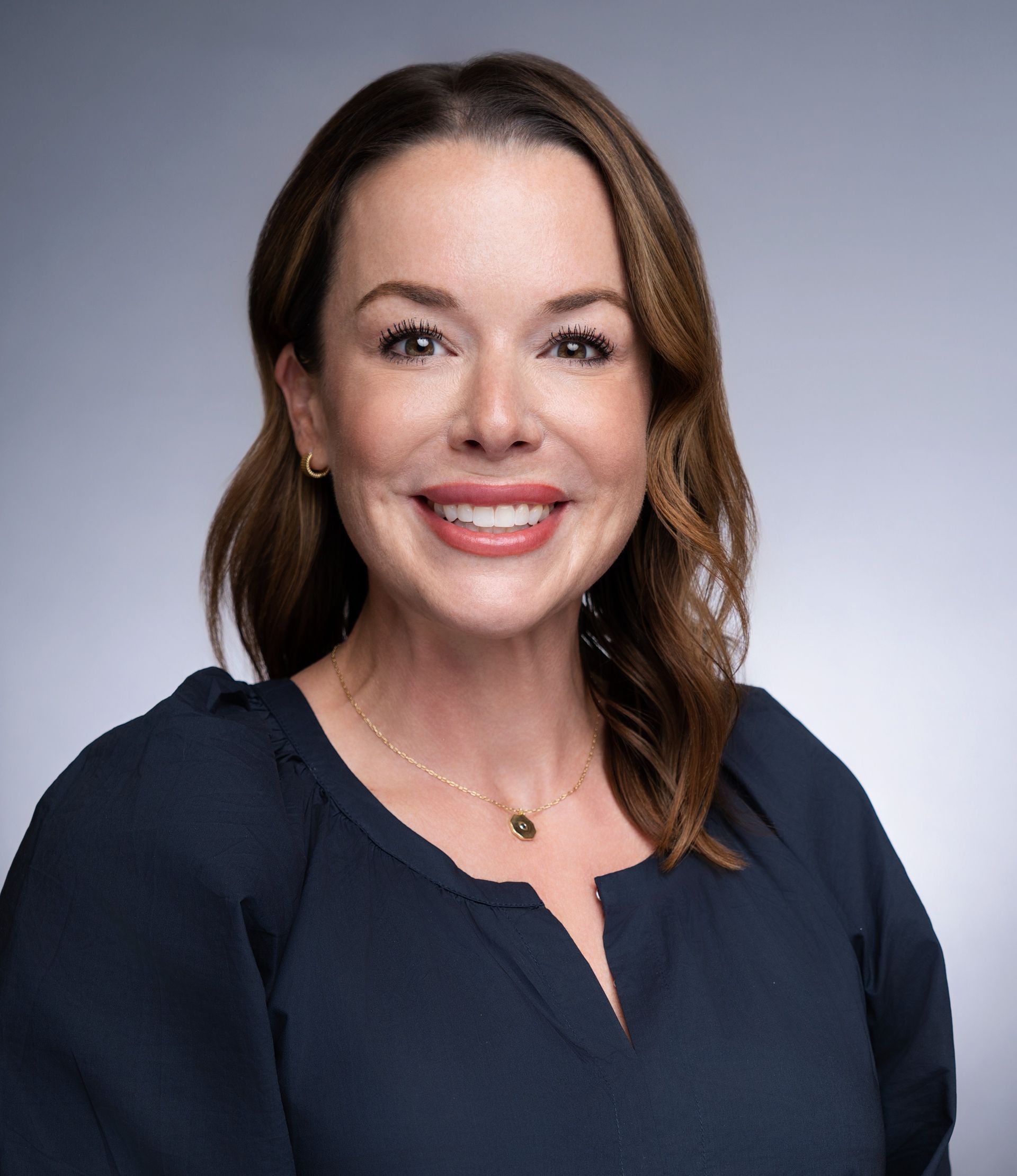 A woman in a blue shirt and necklace is smiling for the camera.