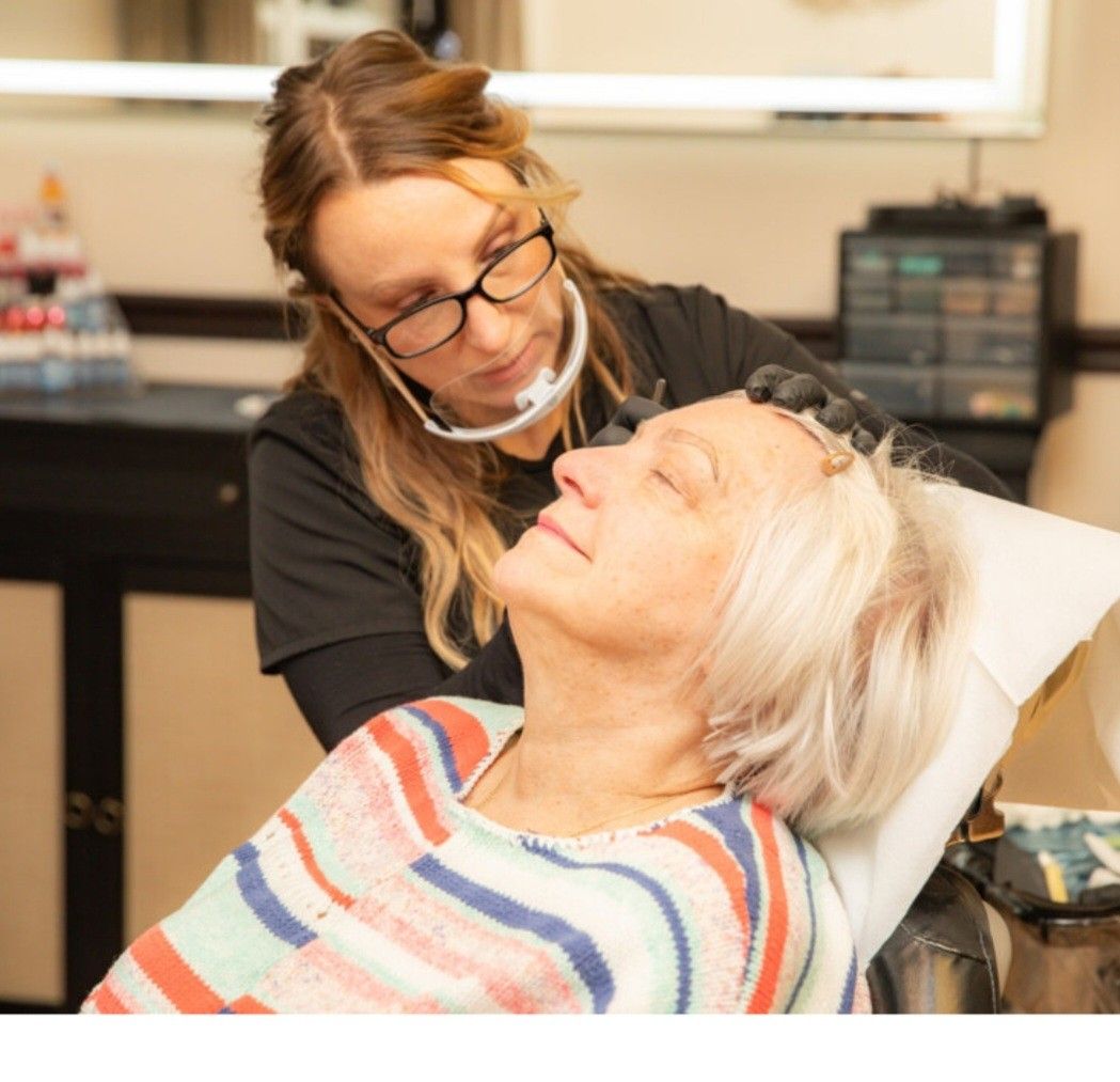 A woman performing a cosmetic procedure on another woman's eyebrow.