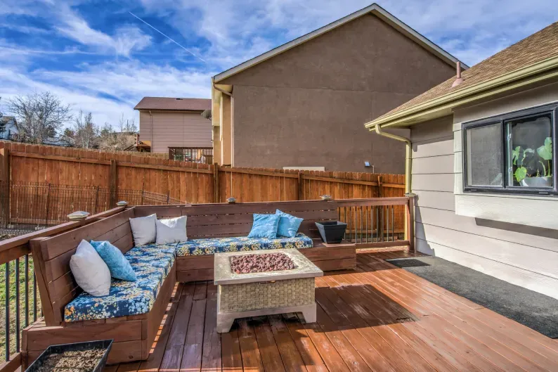 A wooden deck with a couch and a fire pit in front of a house.