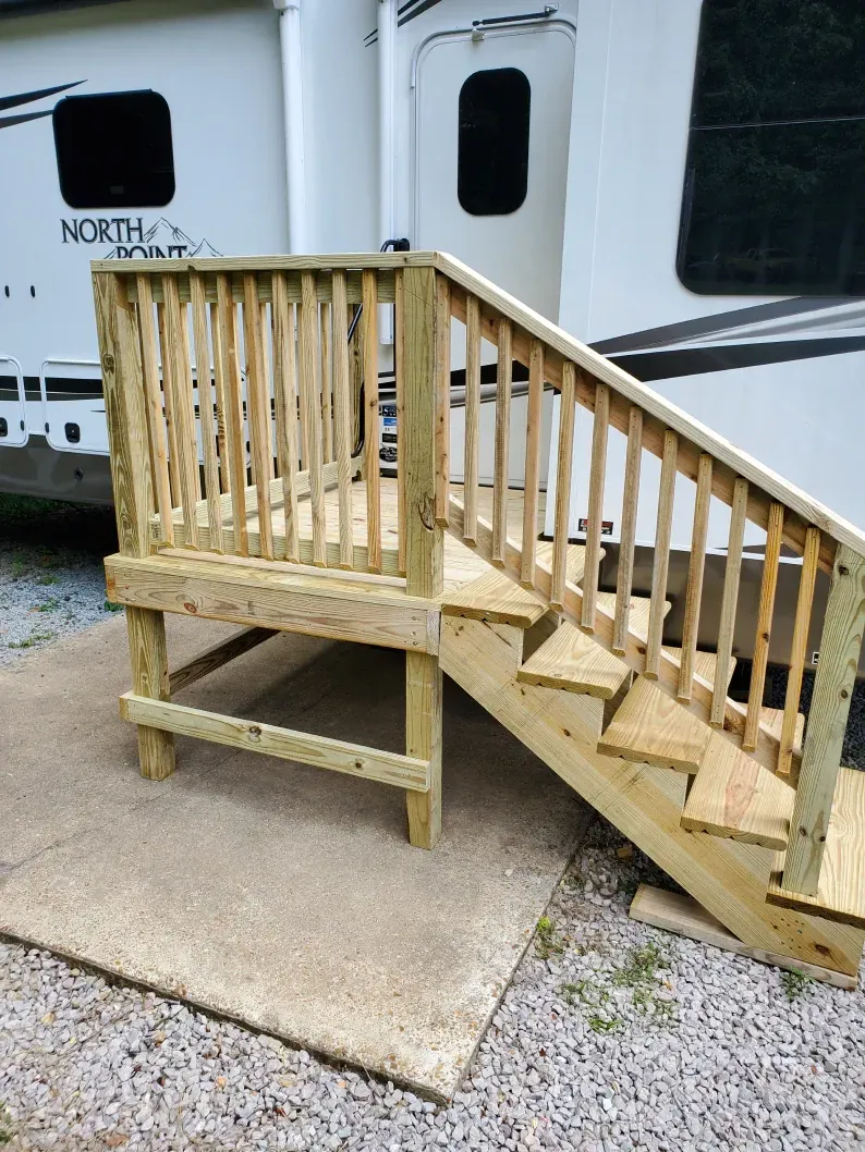 A wooden deck with stairs and railing in front of a trailer.
