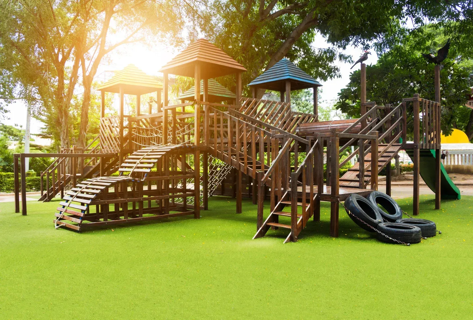 A wooden playground in a park with the sun shining through the trees.