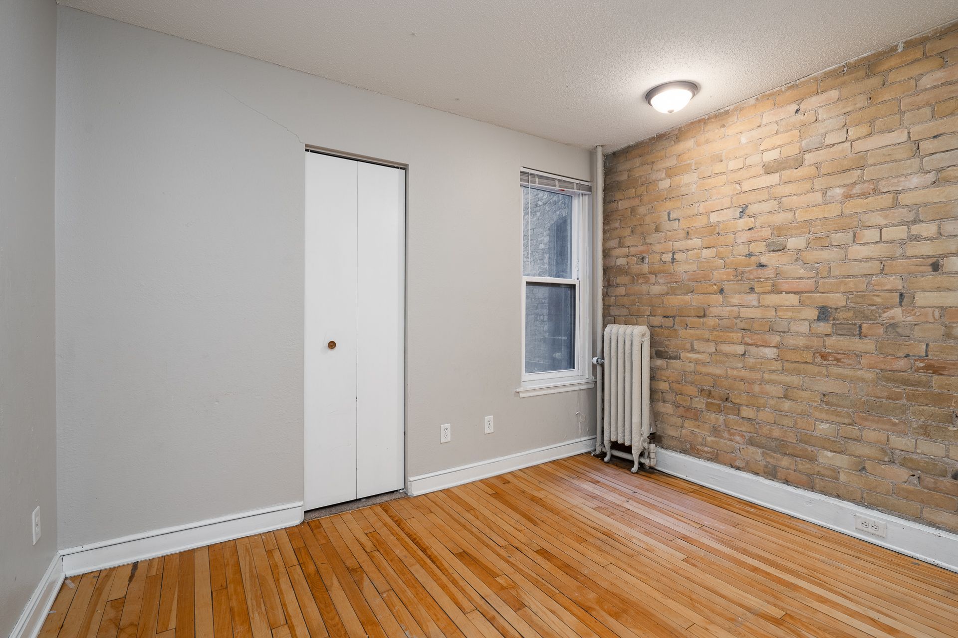 An empty room with hardwood floors and a brick wall.