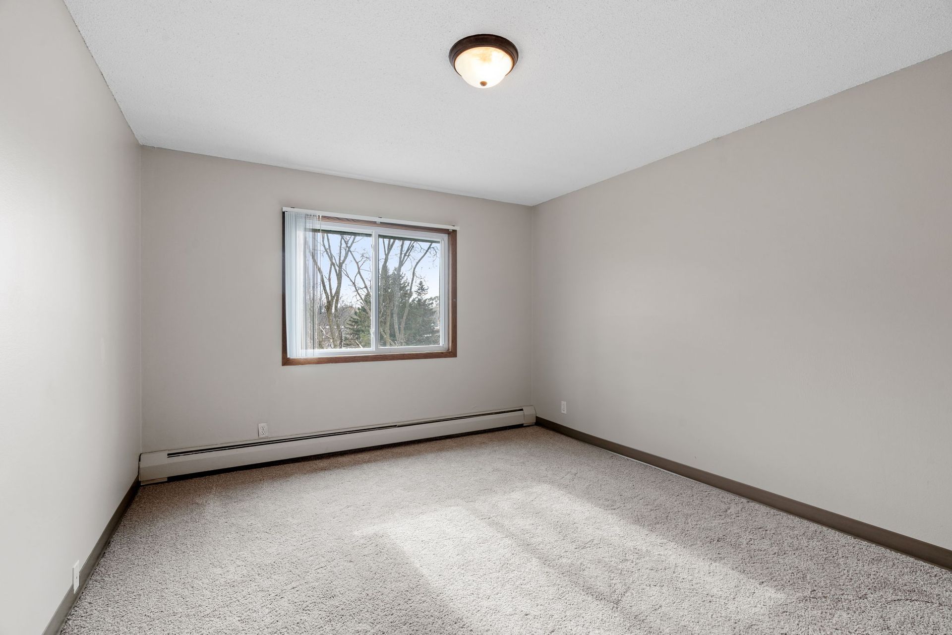 An empty bedroom with a window and a ceiling light.