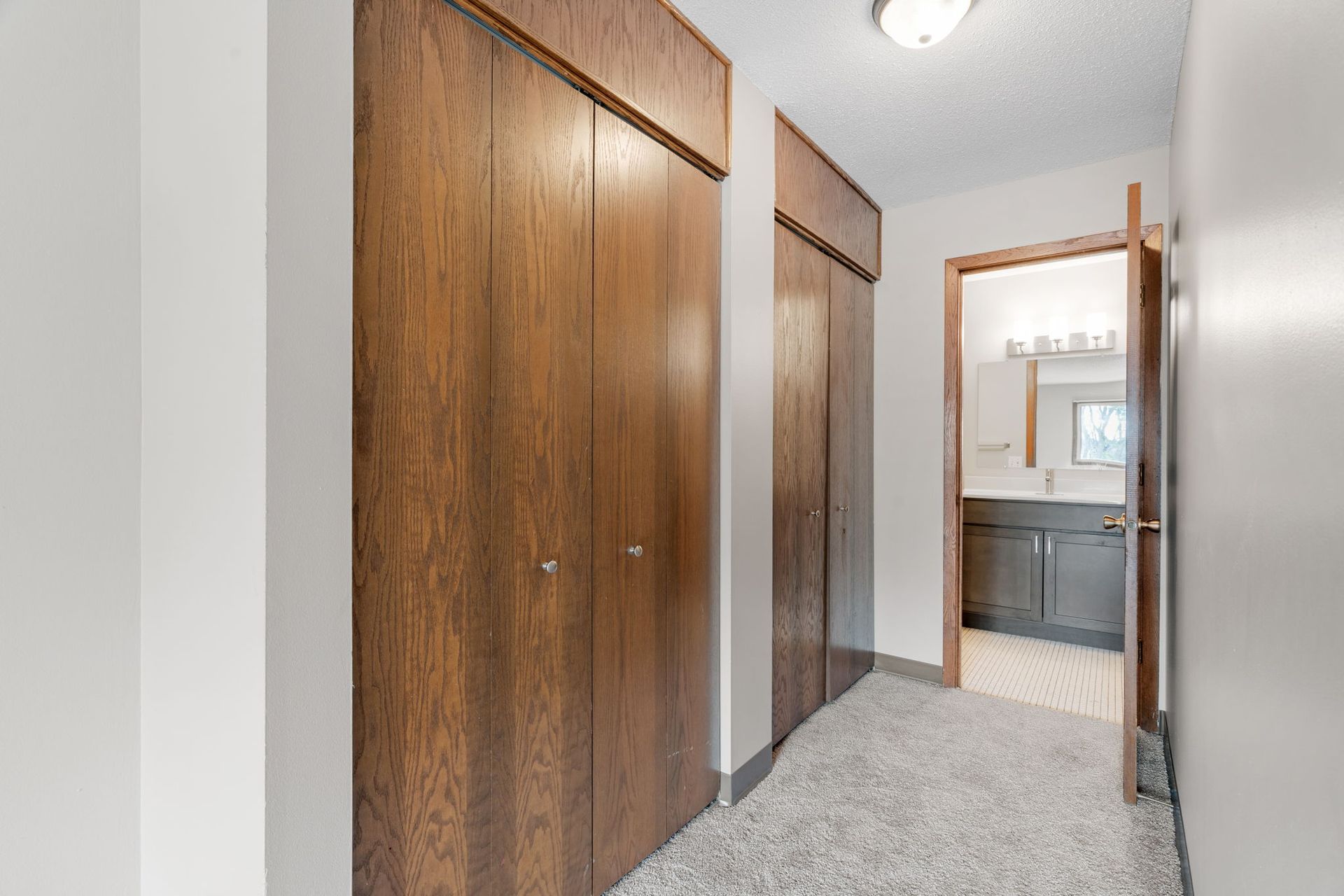 A hallway with wooden cabinets and a bathroom in the background.