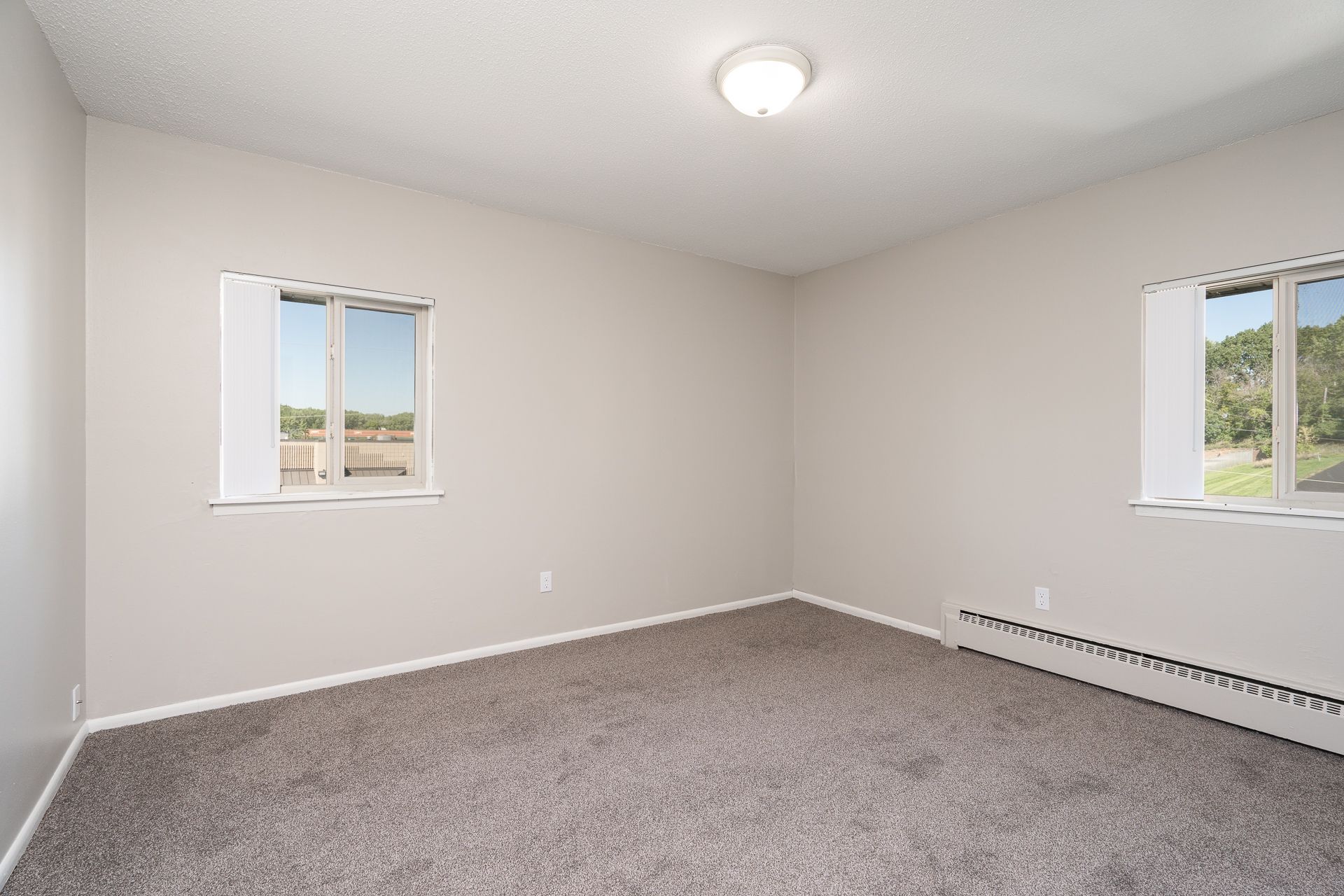An empty bedroom with a carpeted floor and two windows.