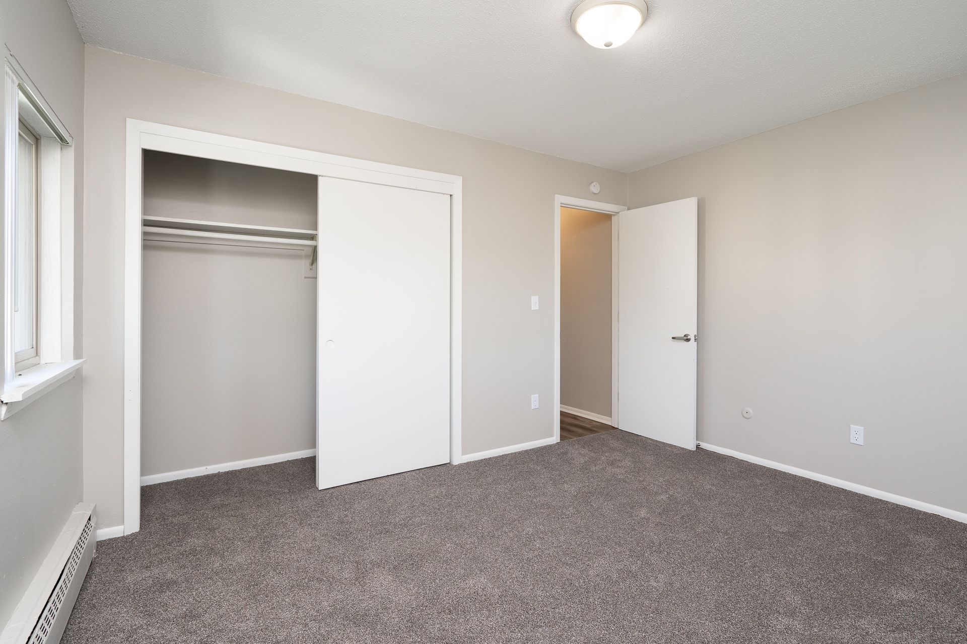 An empty bedroom with a closet and a window.