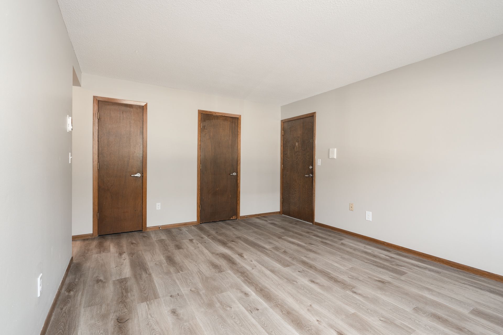 An empty living room with hardwood floors and two doors.