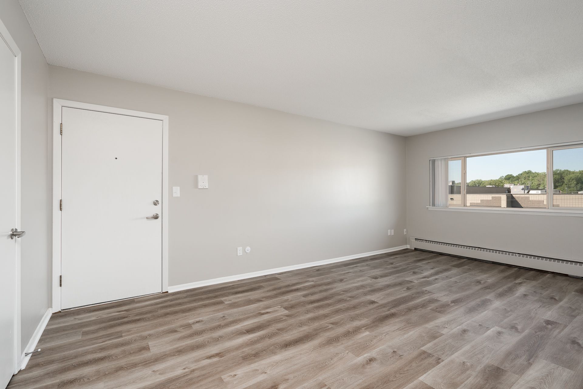 An empty living room with hardwood floors and a large window.