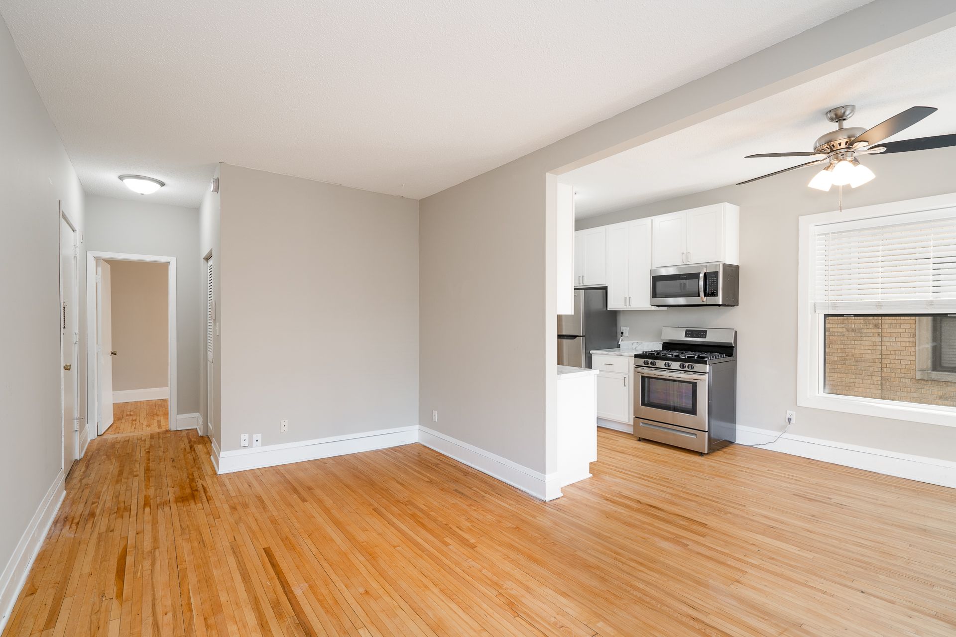 A living room with hardwood floors and a ceiling fan next to a kitchen.