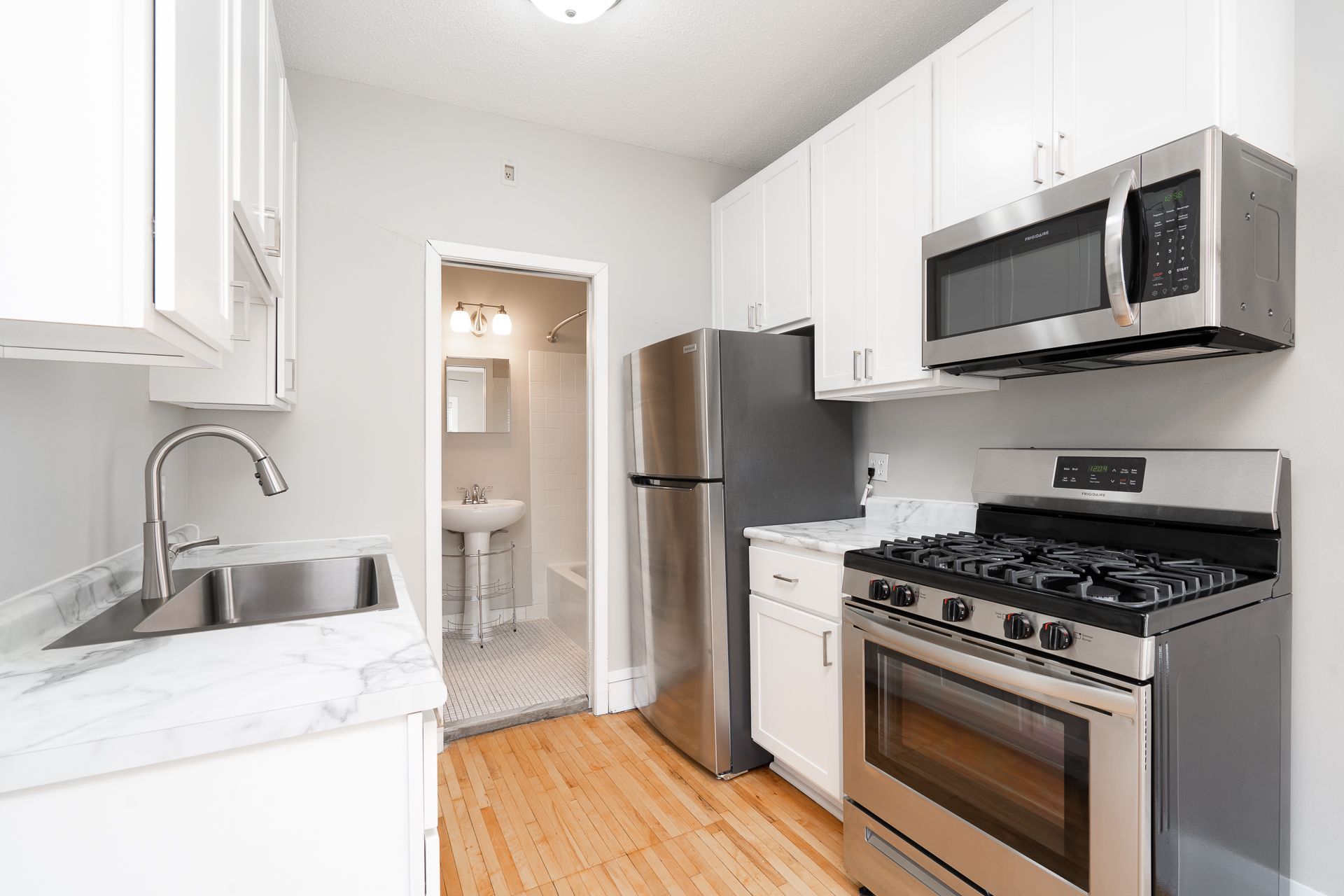 A kitchen with a stove , refrigerator , microwave and sink.