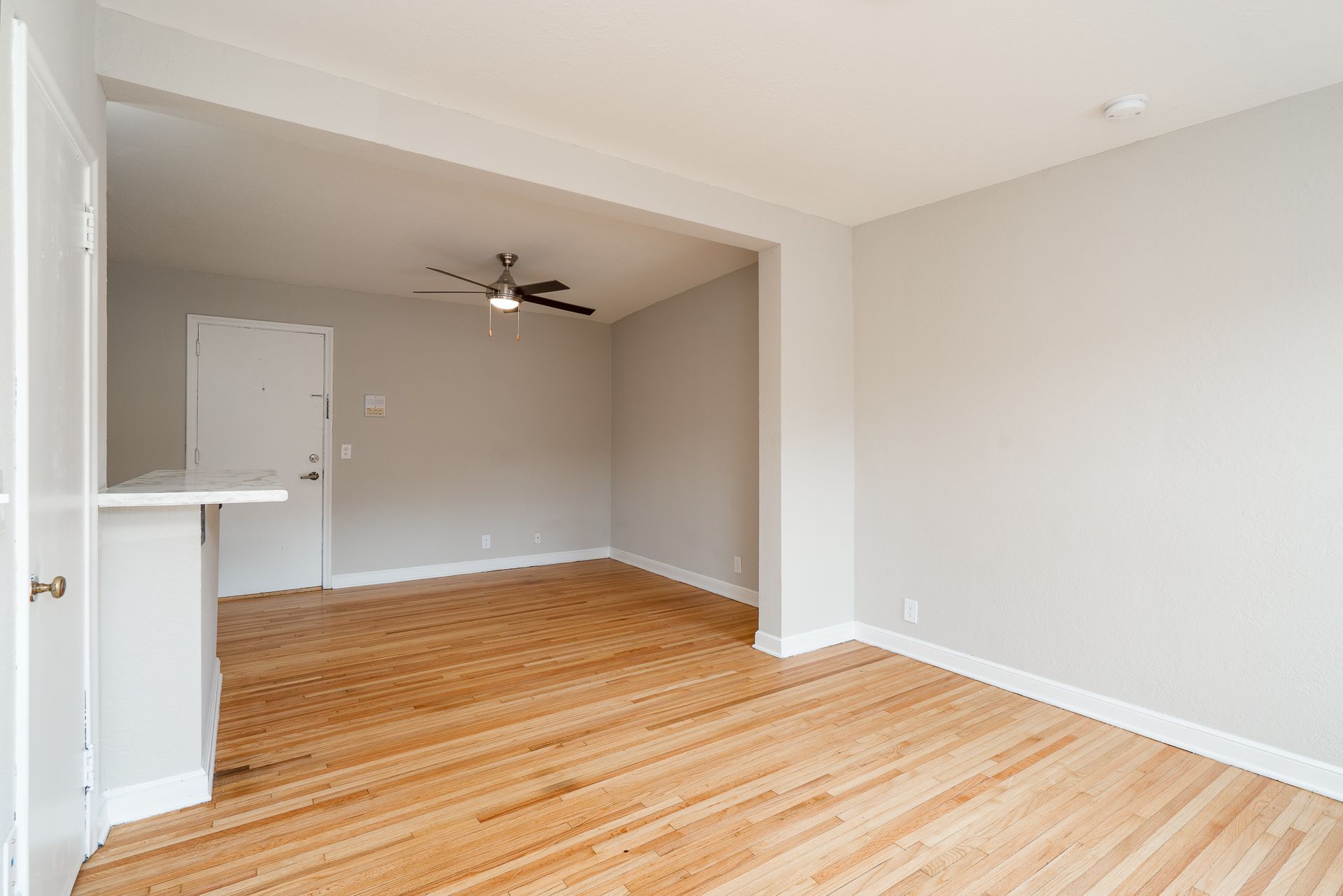 An empty living room with hardwood floors and a ceiling fan.