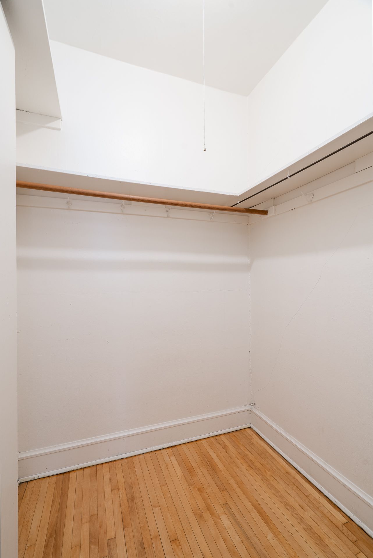 An empty walk in closet with hardwood floors and white walls
