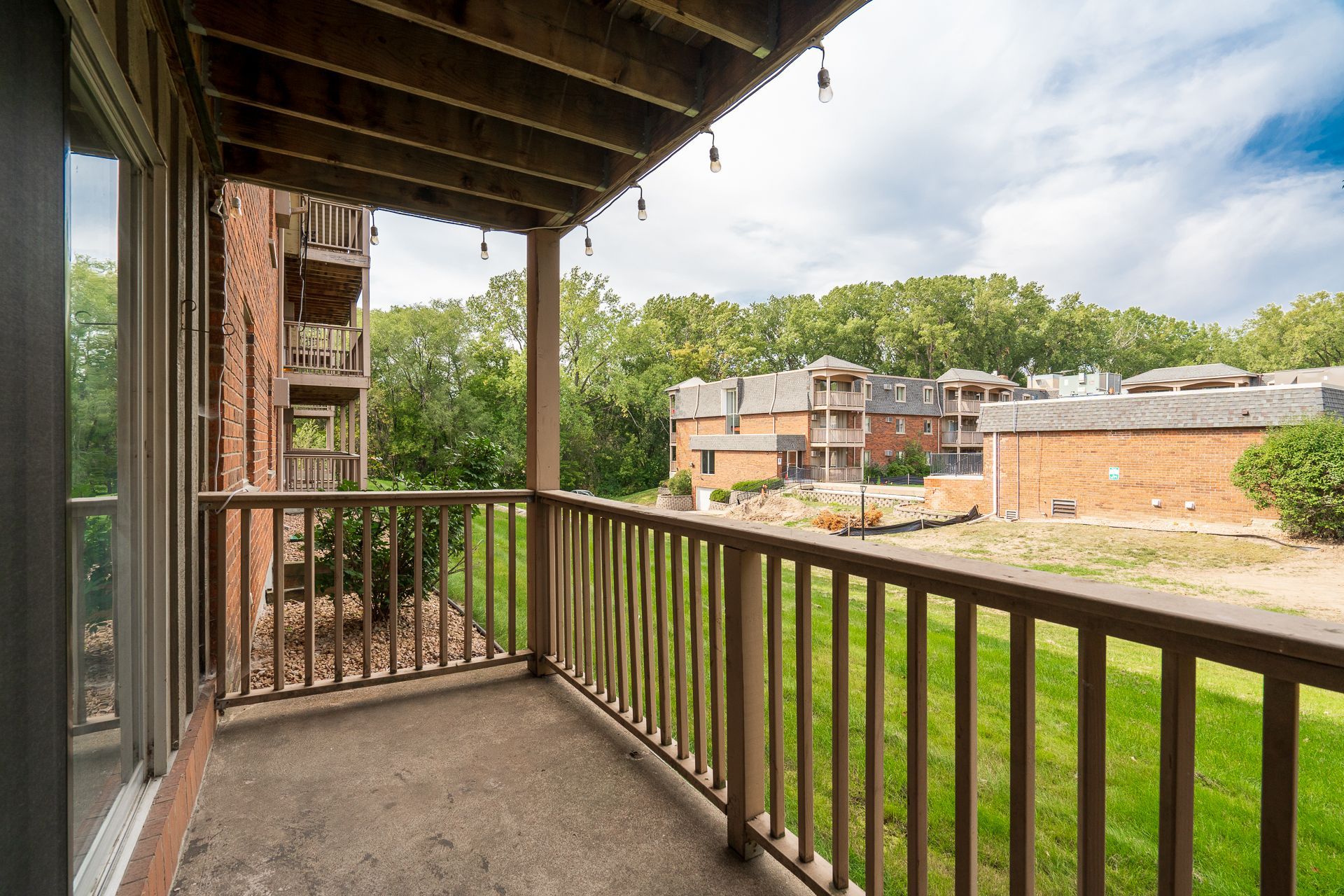 A balcony with a wooden railing overlooking a lush green field.
