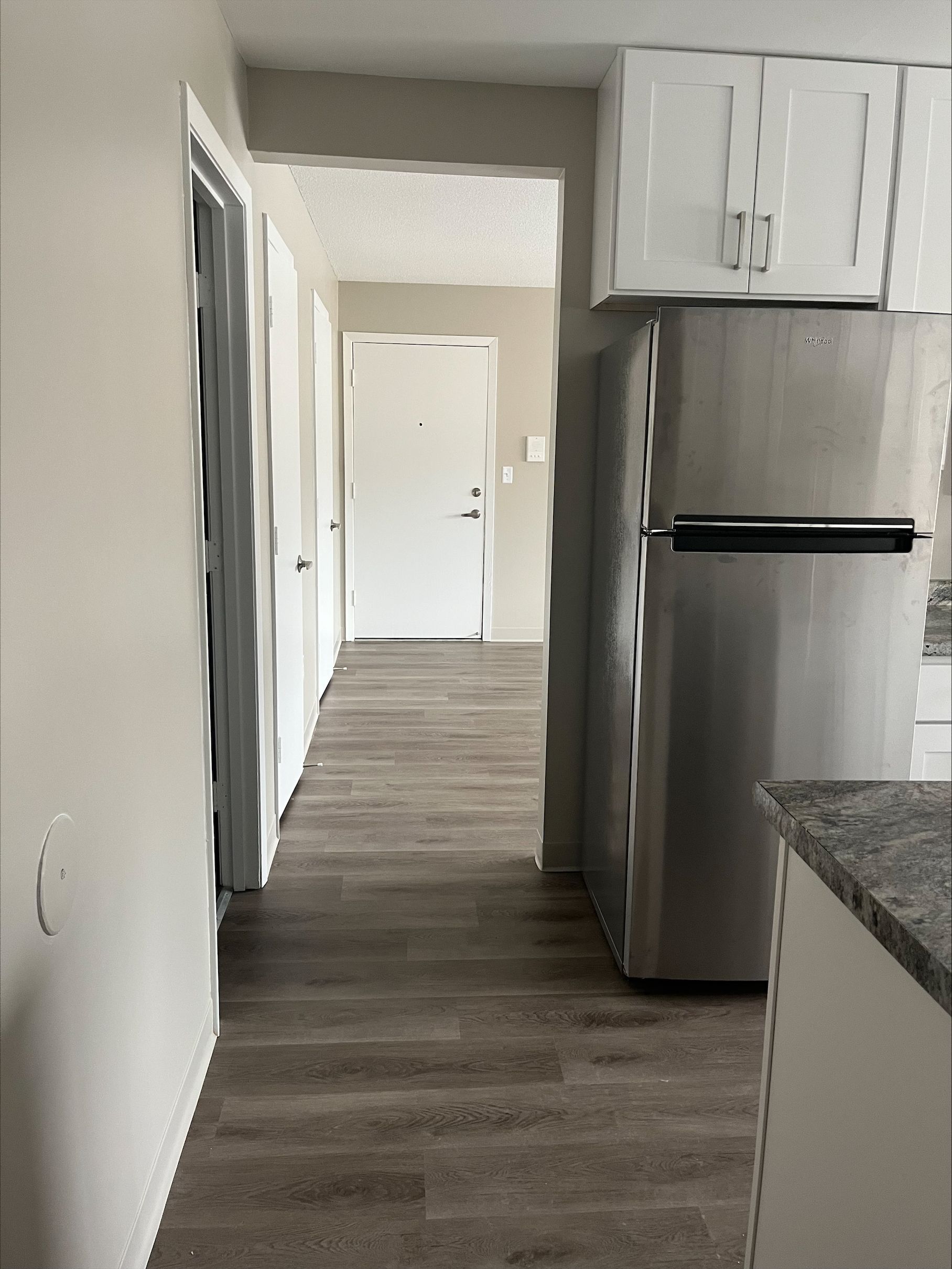 A hallway leading to a kitchen with a stainless steel refrigerator.