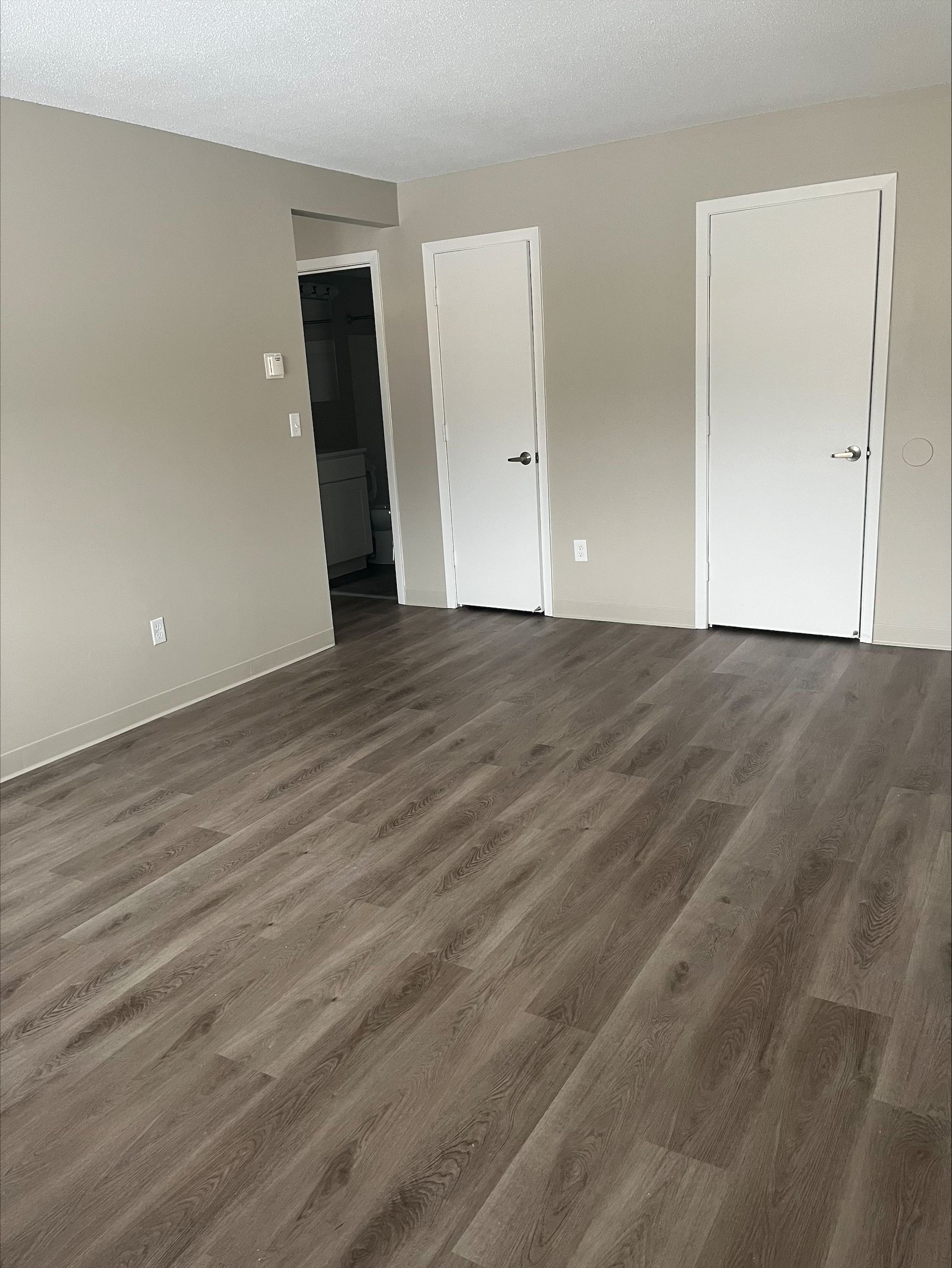 An empty living room with hardwood floors and white doors.
