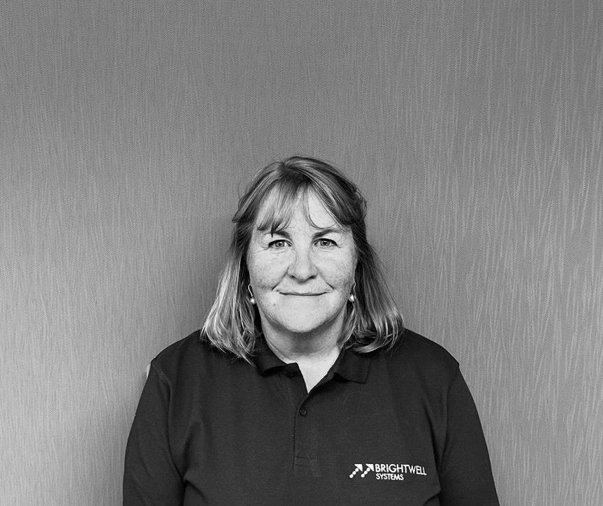 Woman in a dark polo shirt smiles, posing in front of a textured wall.