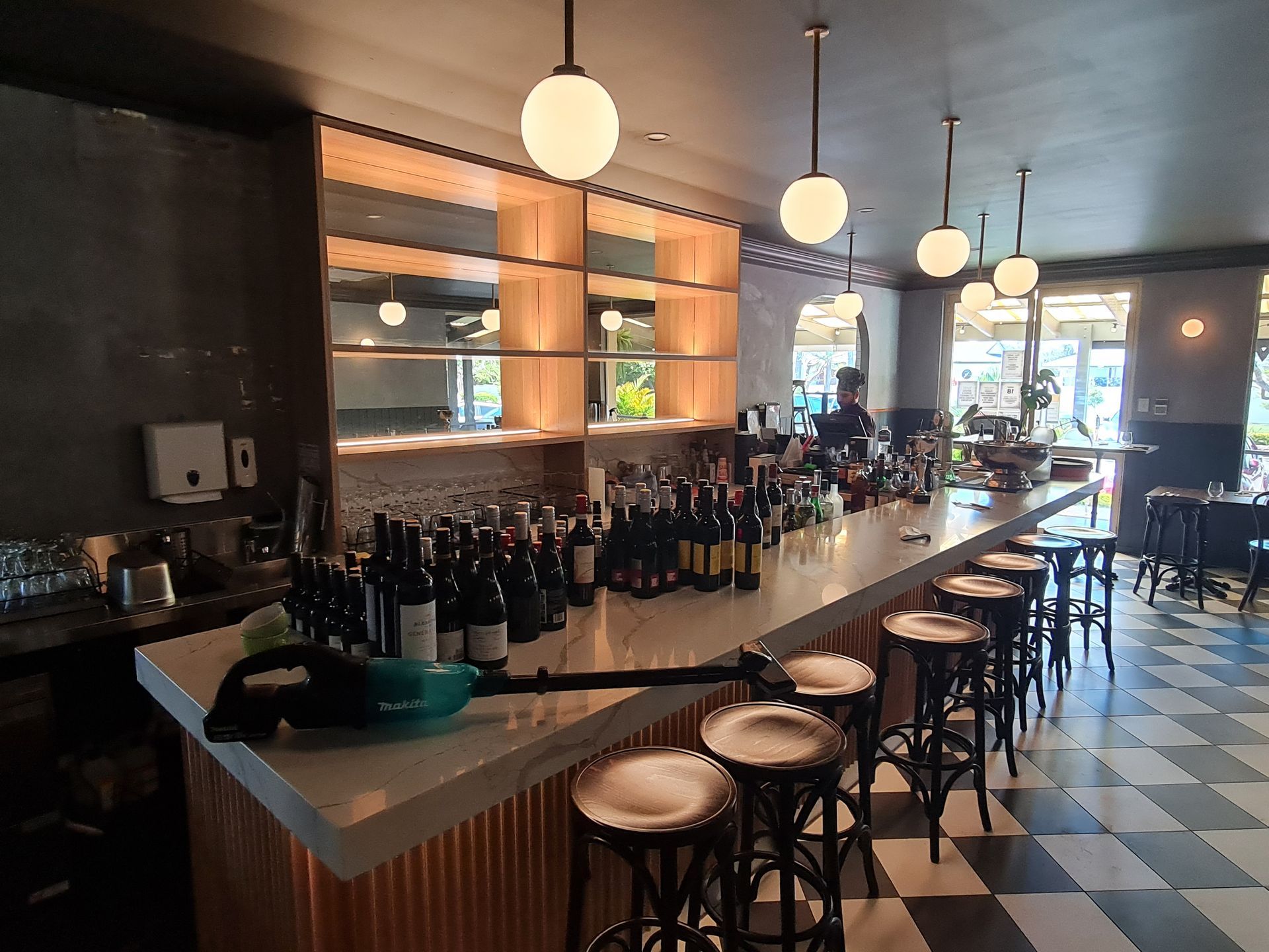 Stylish bar interior with a long counter, stools, hanging globe lights, and bottles on display