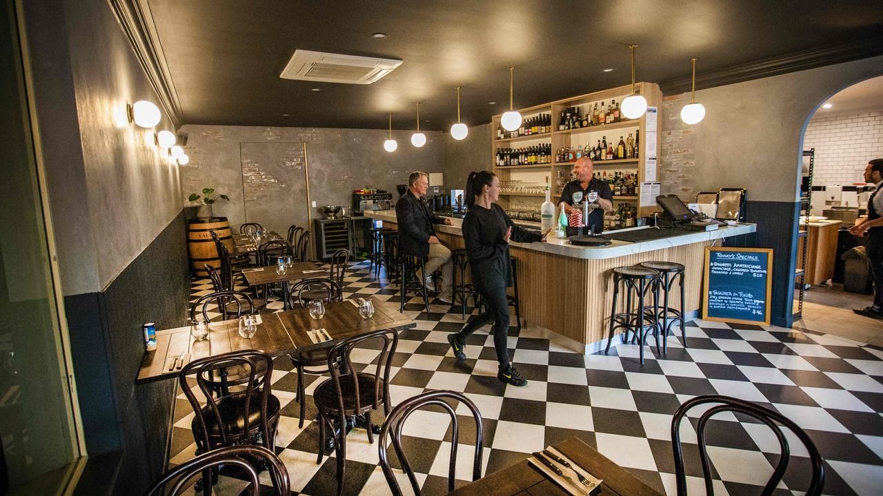 Cozy café with checkered floor, bar counter, tables, and a few people inside under warm lighting