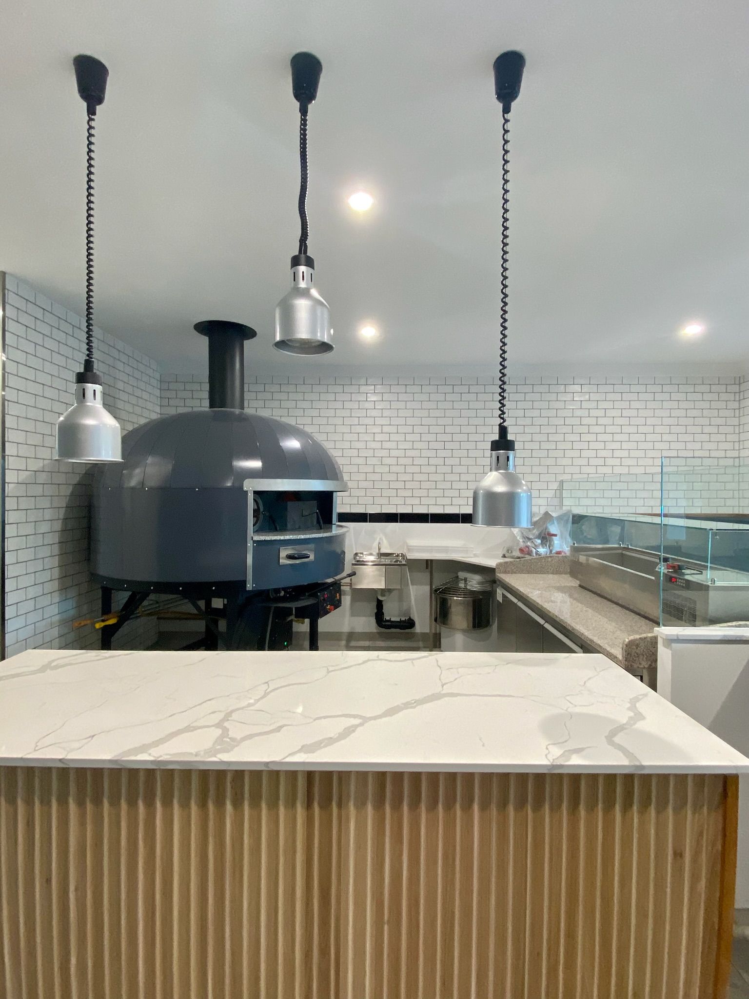 Modern pizzeria interior with a large oven, hanging lights, and a marble-topped counter