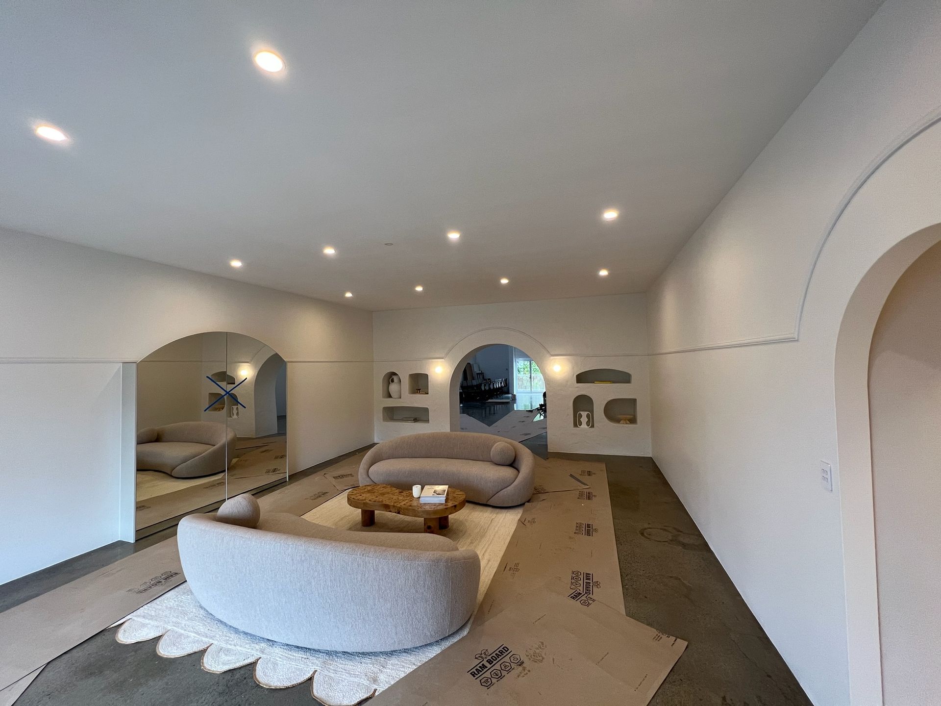Modern minimalist living room with curved beige sofa, low tables, recessed lights, and arched doorways