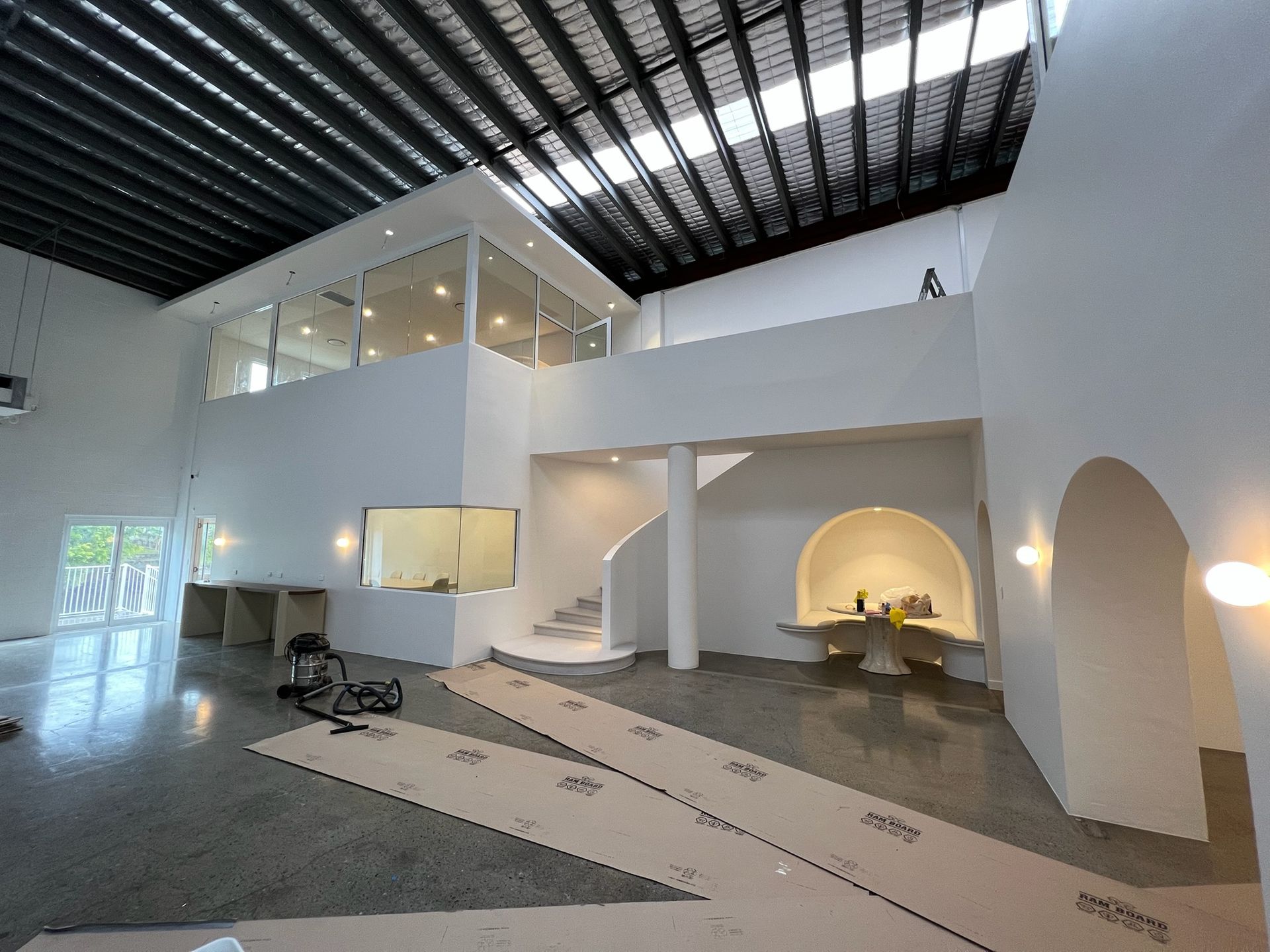 Modern white interior with arches, staircase, mezzanine, and a high black slatted ceiling