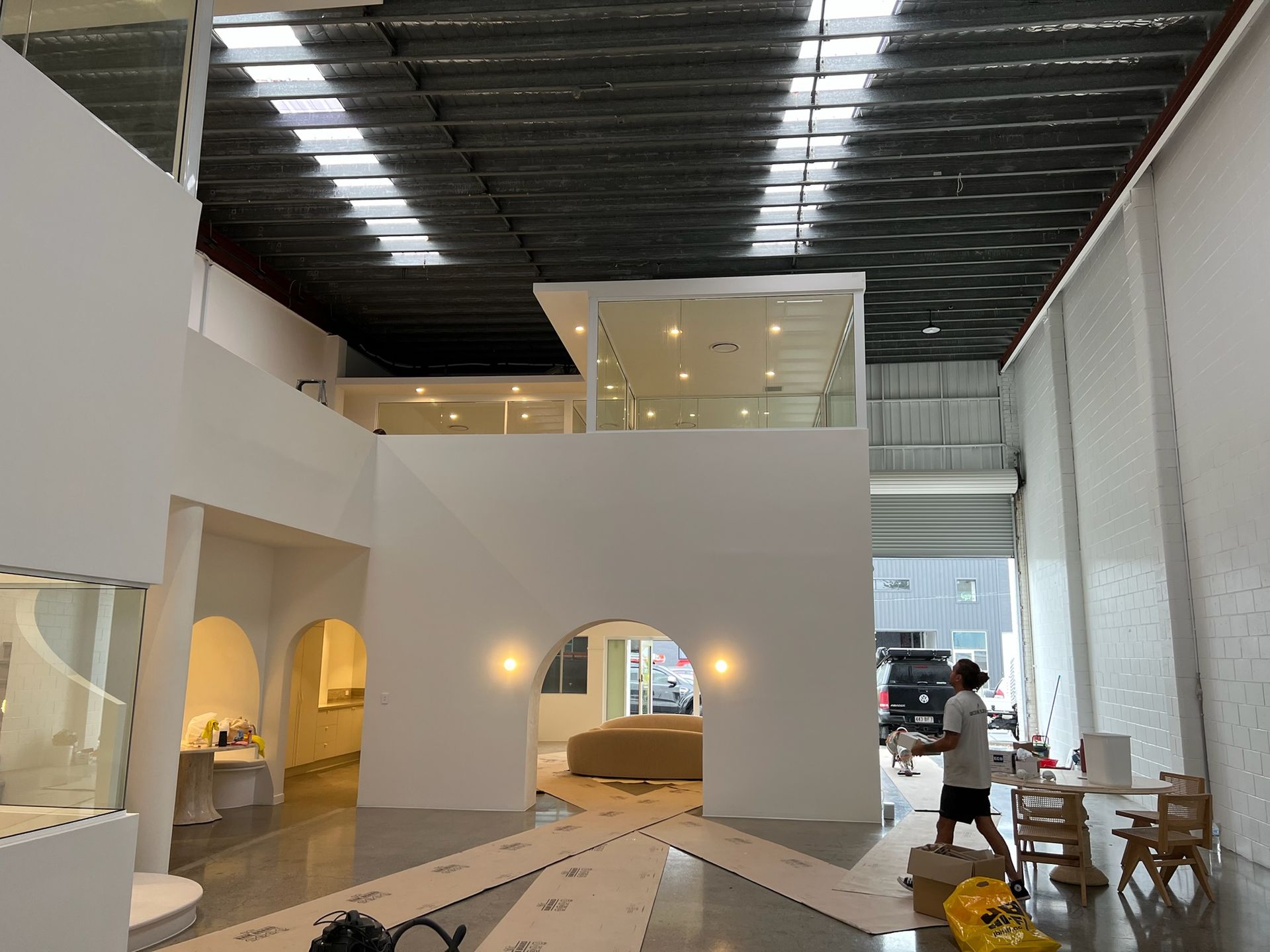 Modern white interior with arched openings, warm lights, and a loft under a dark ceiling in a showroom.