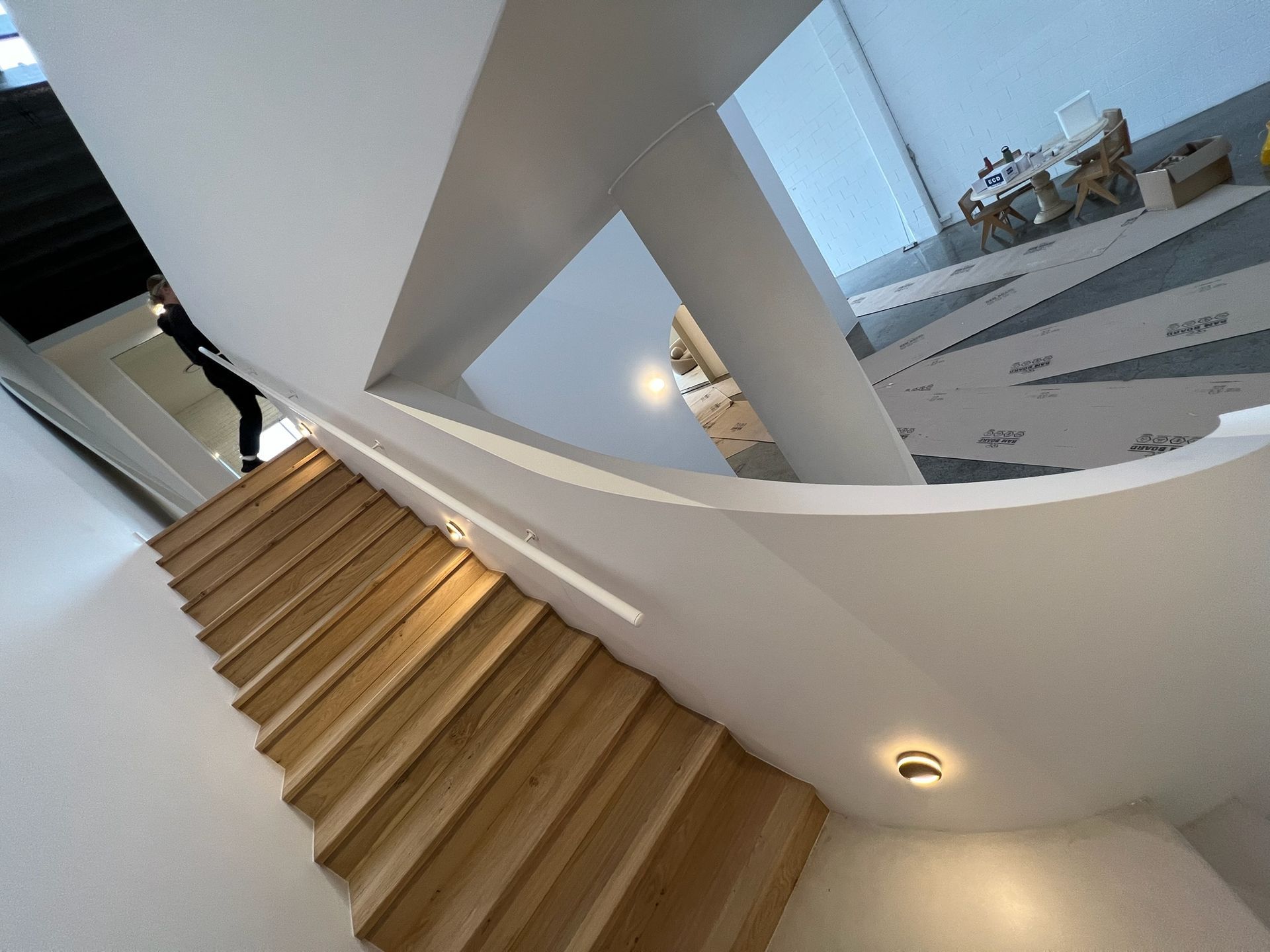 Curved indoor staircase with wooden steps and white walls in a modern unfinished building.
