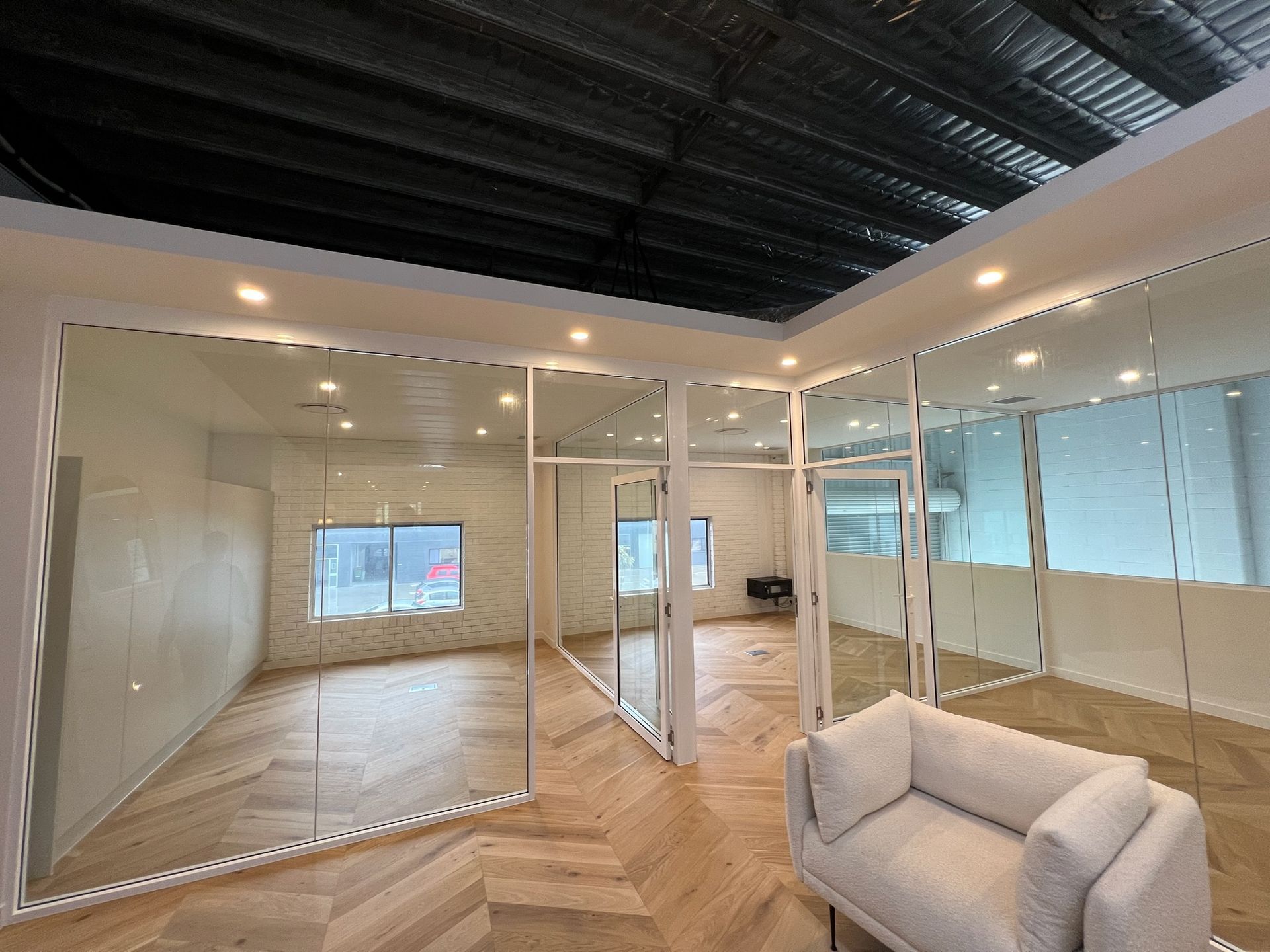 Empty modern office with glass walls, herringbone wood floor, and a light gray sofa