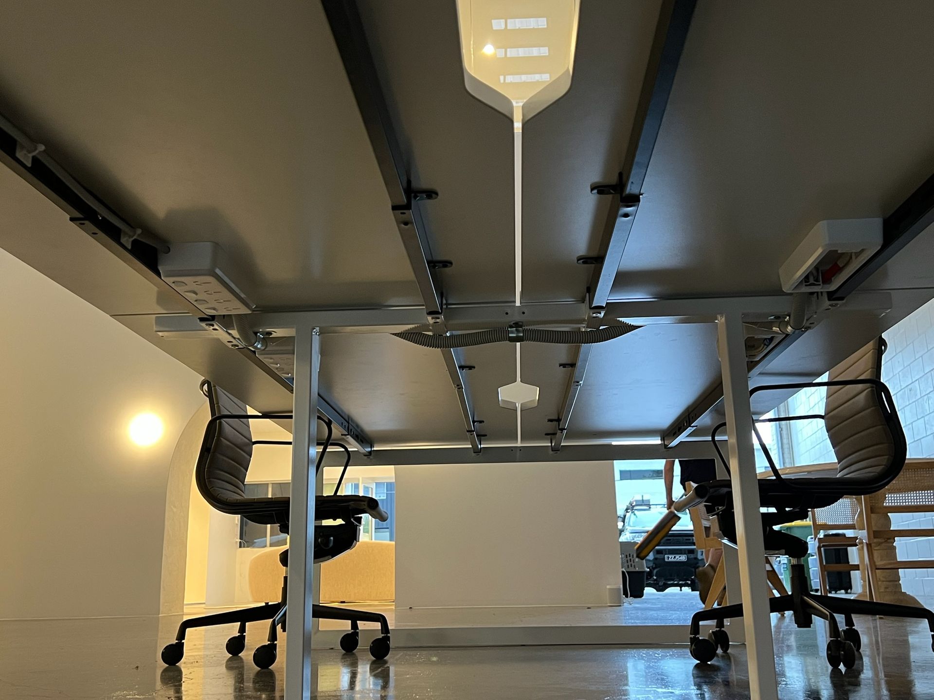 Under a conference table, showing chairs, cables, and a bright room beyond