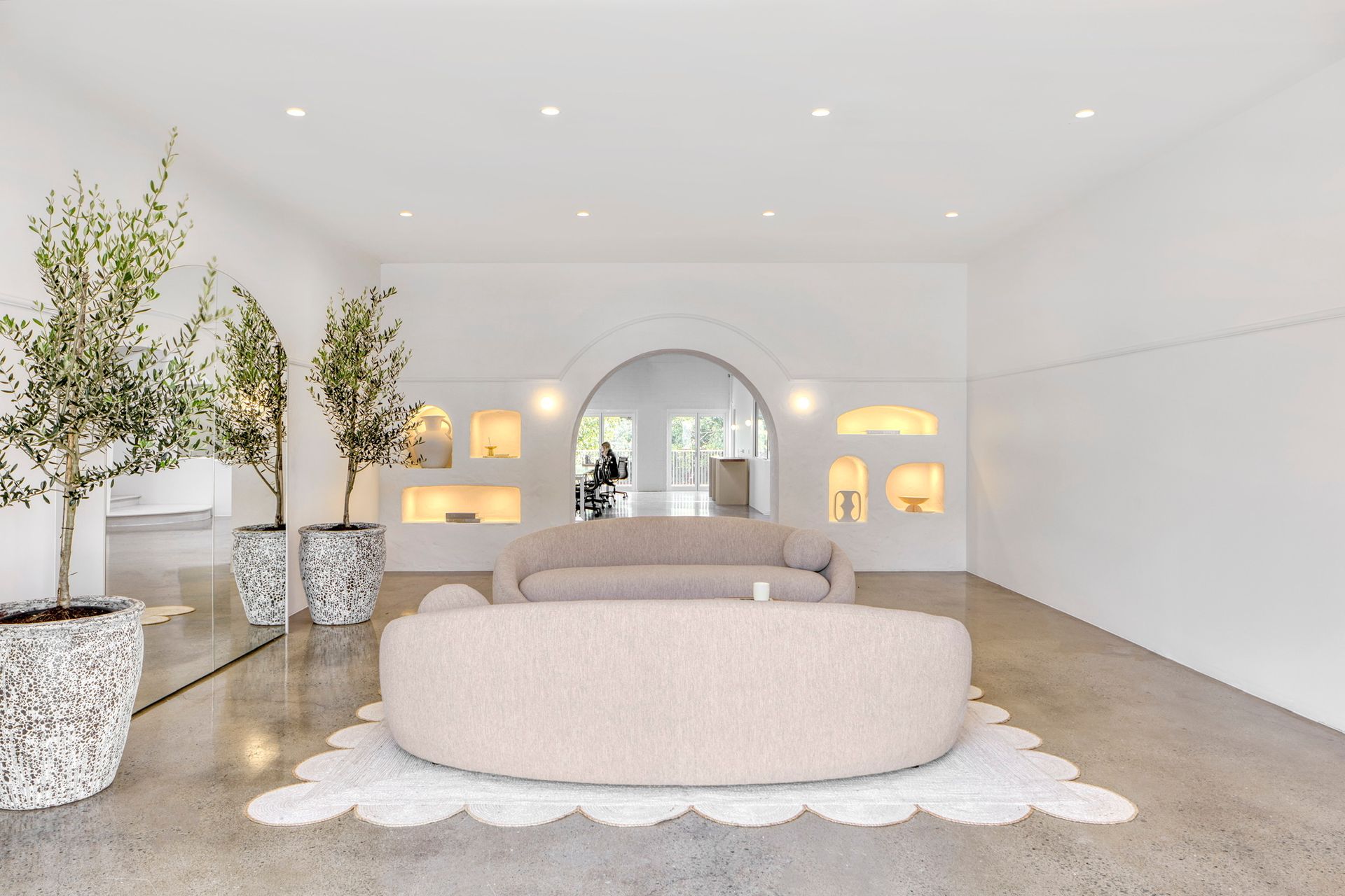 Bright minimalist living room with a blush round sofa, potted trees, and arched mirror accents