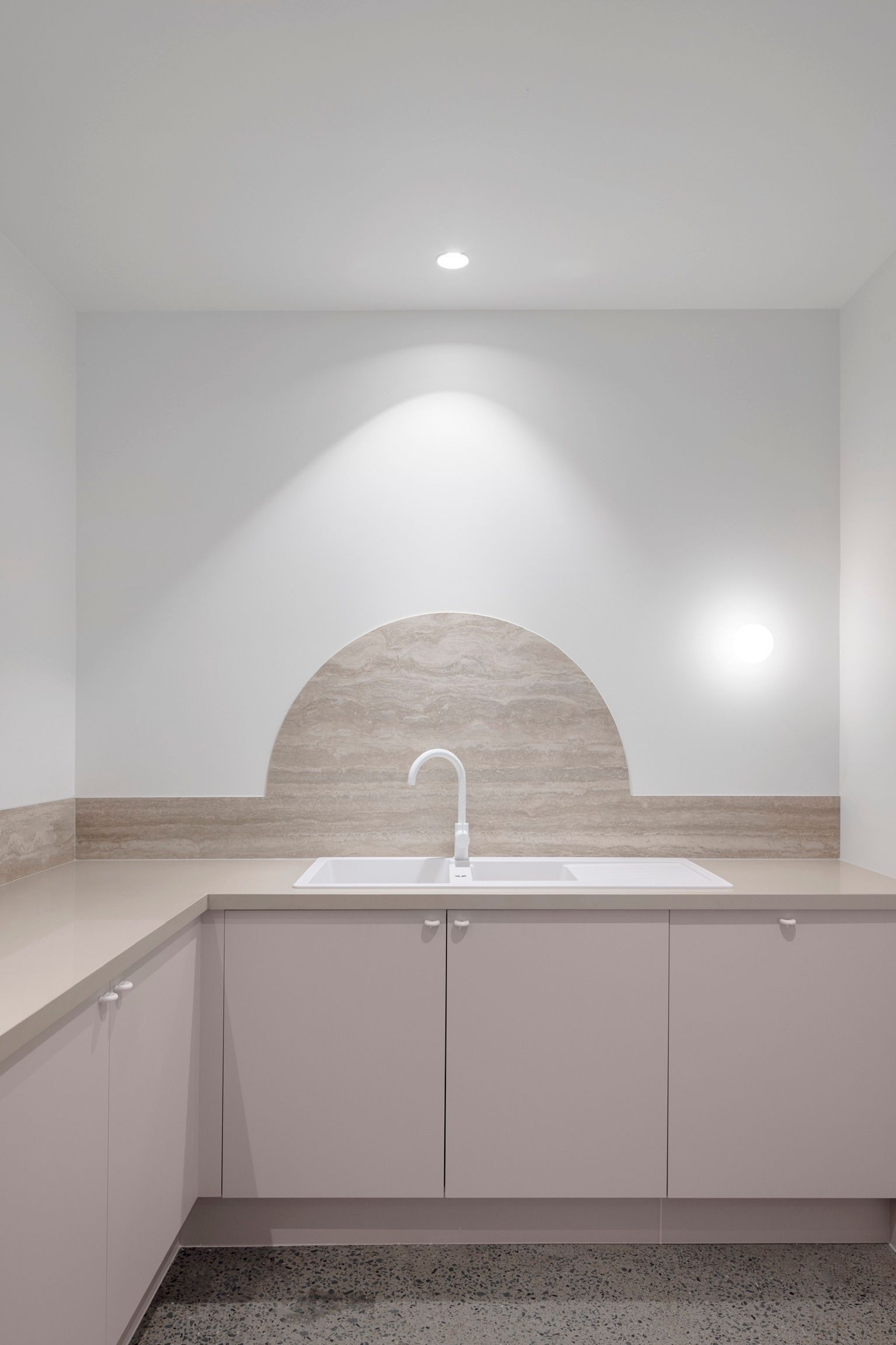 Minimal white kitchen with beige countertops, a sink, and arched backsplash lighting