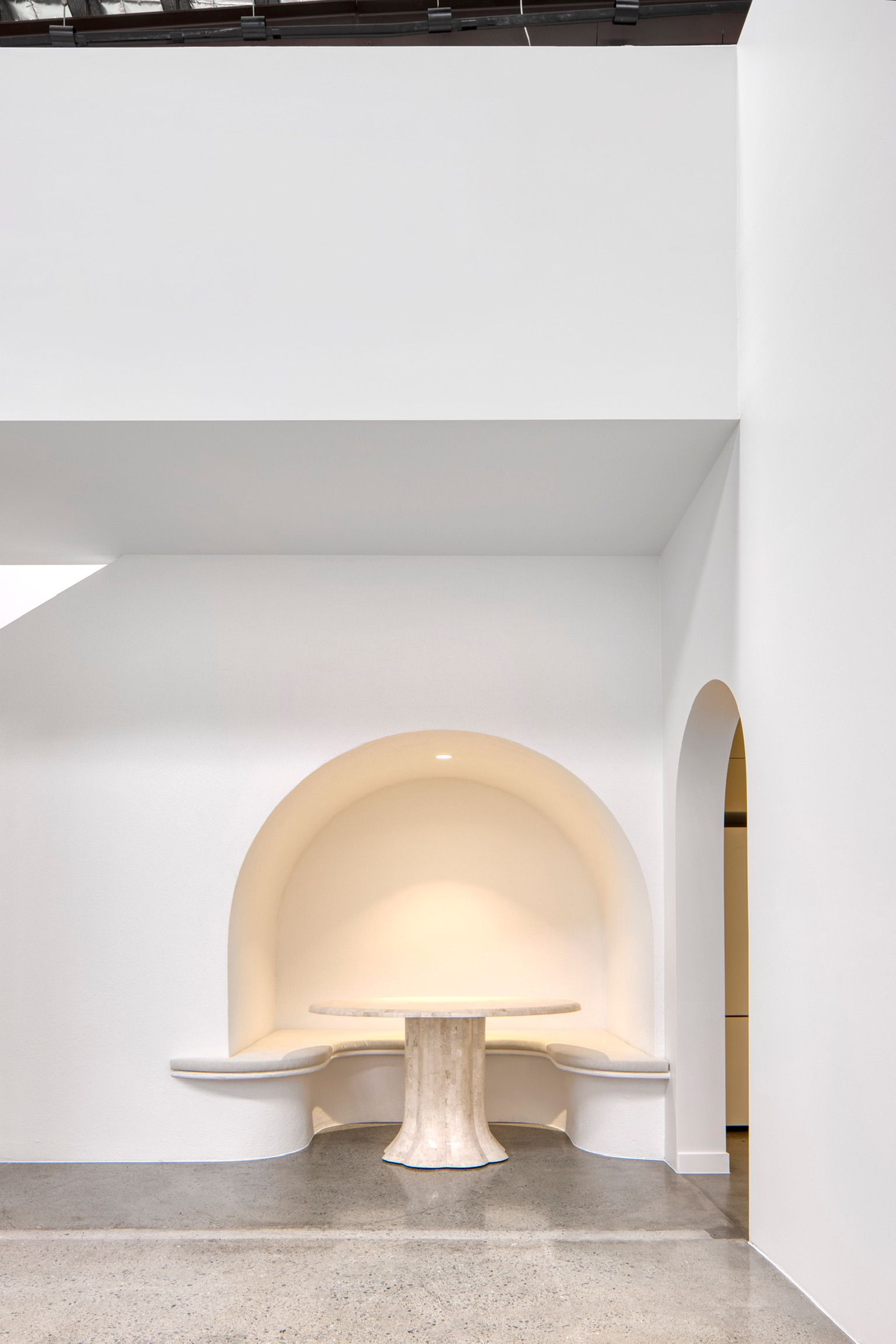 Minimalist white interior with a built-in arched niche seating area and round tables on a speckled floor