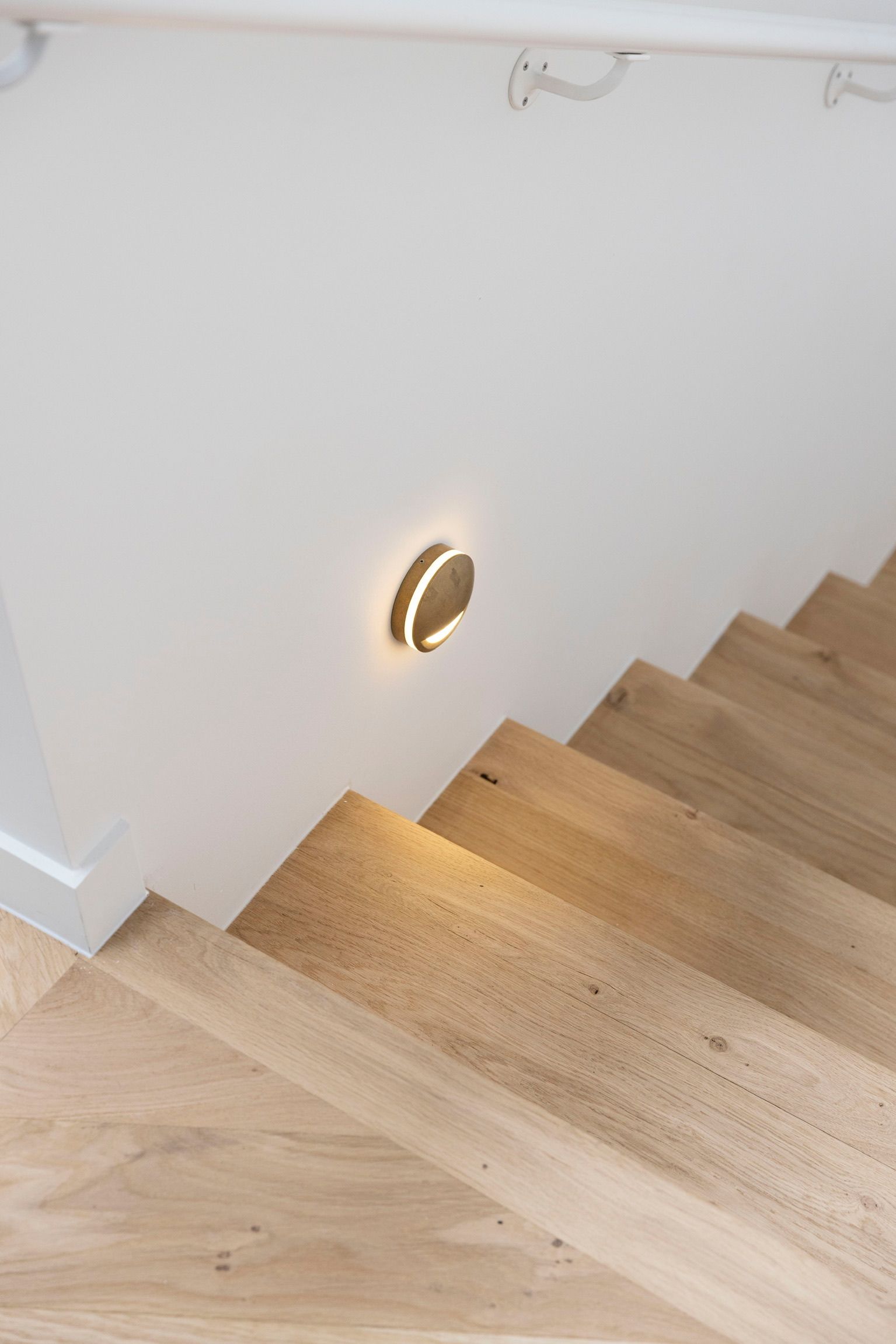 Lit stairway with a recessed wall light and light wood steps.