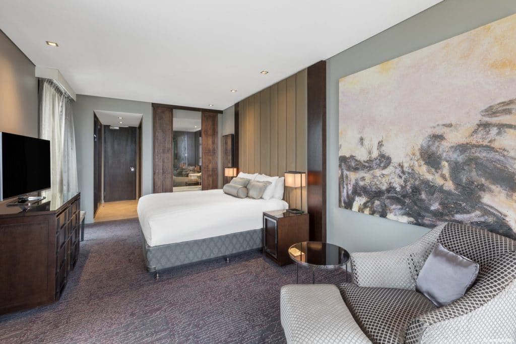 Modern hotel room with a bed, sitting chair, large wall art, and neutral decor