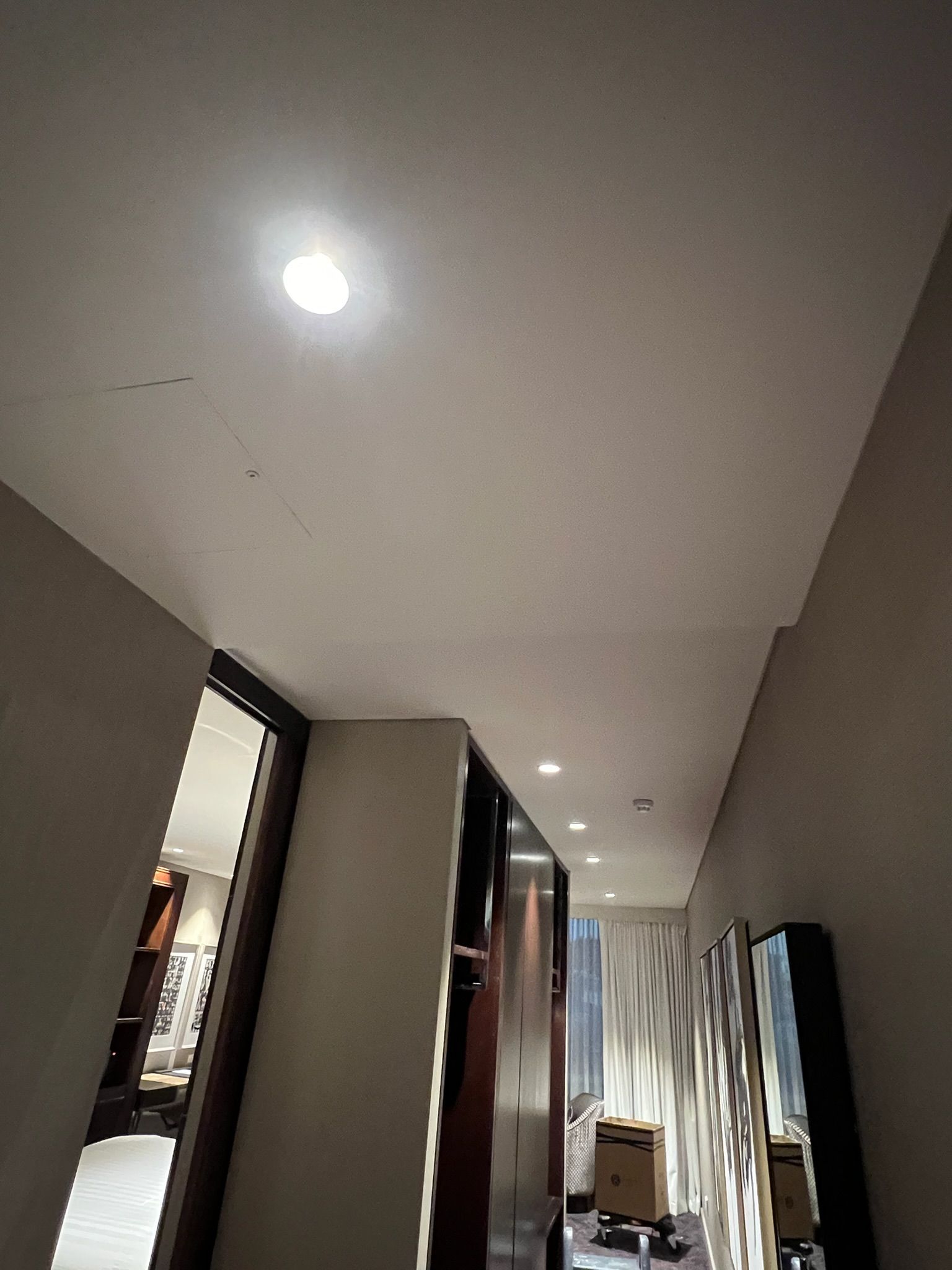 Narrow hallway with recessed ceiling lights, mirrors, and a doorway at the end