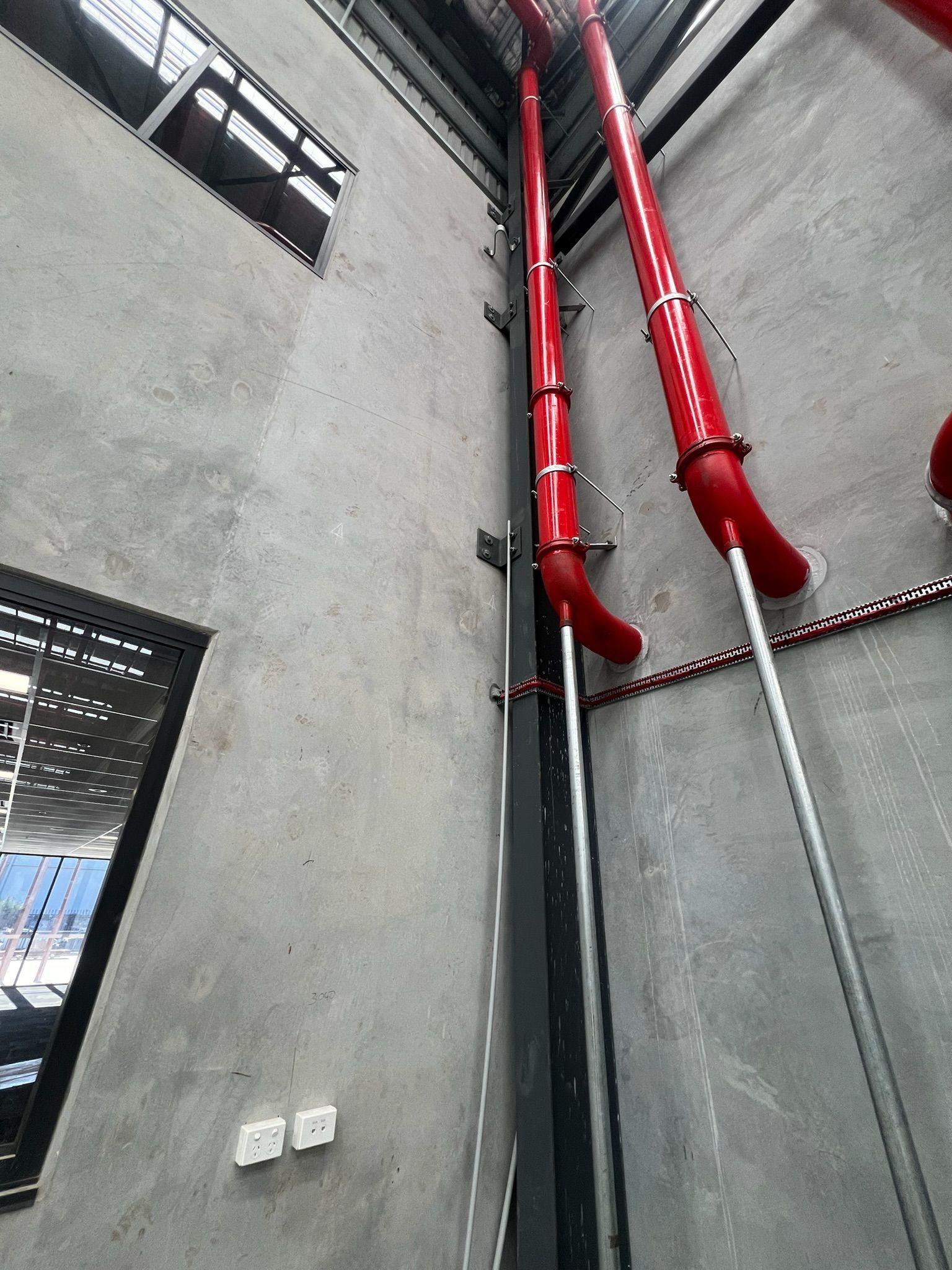 Gray industrial wall with red fire sprinkler pipes running up to the ceiling