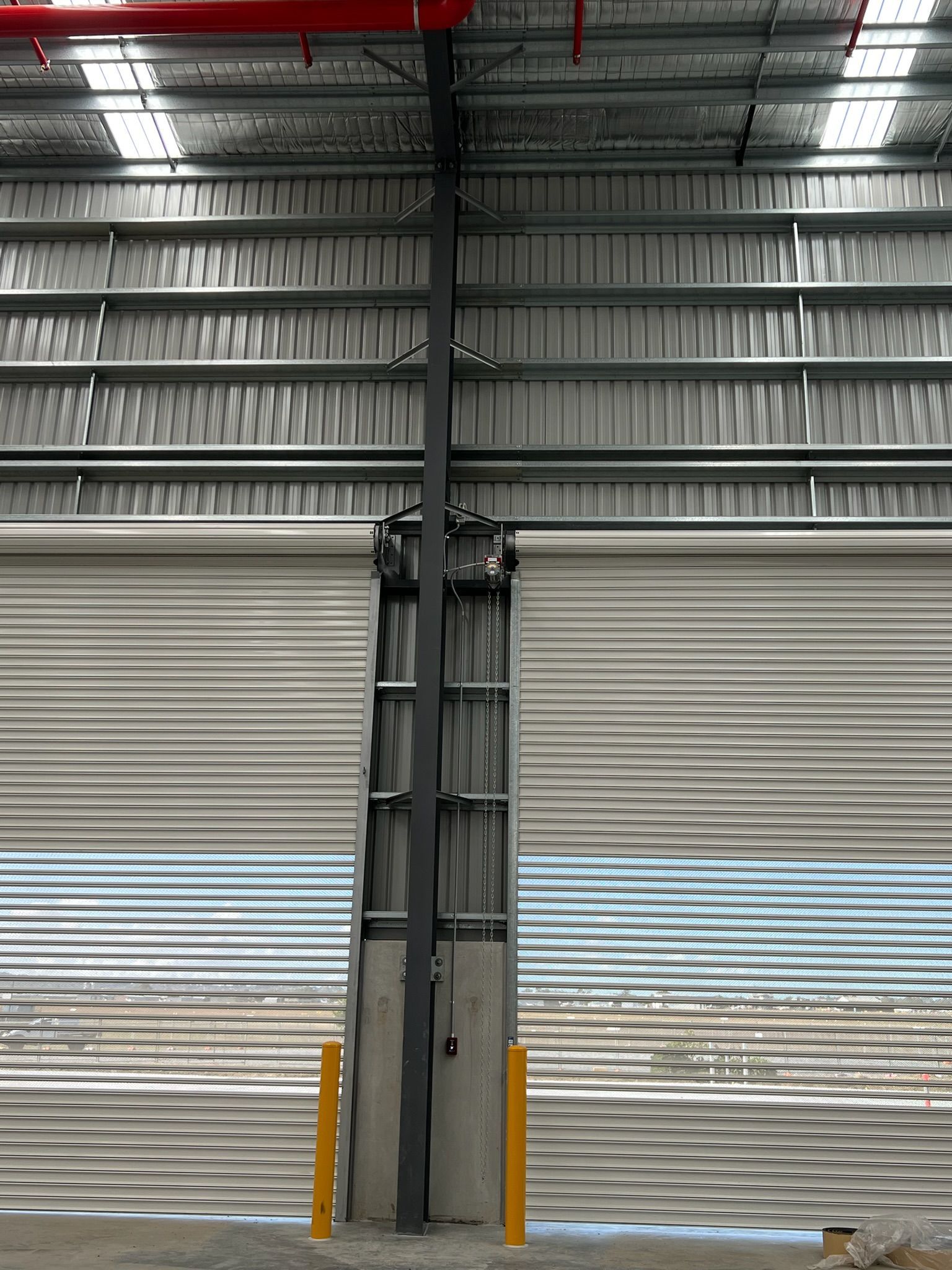 Industrial warehouse interior with closed roll-up doors, steel beams, and yellow safety bollards