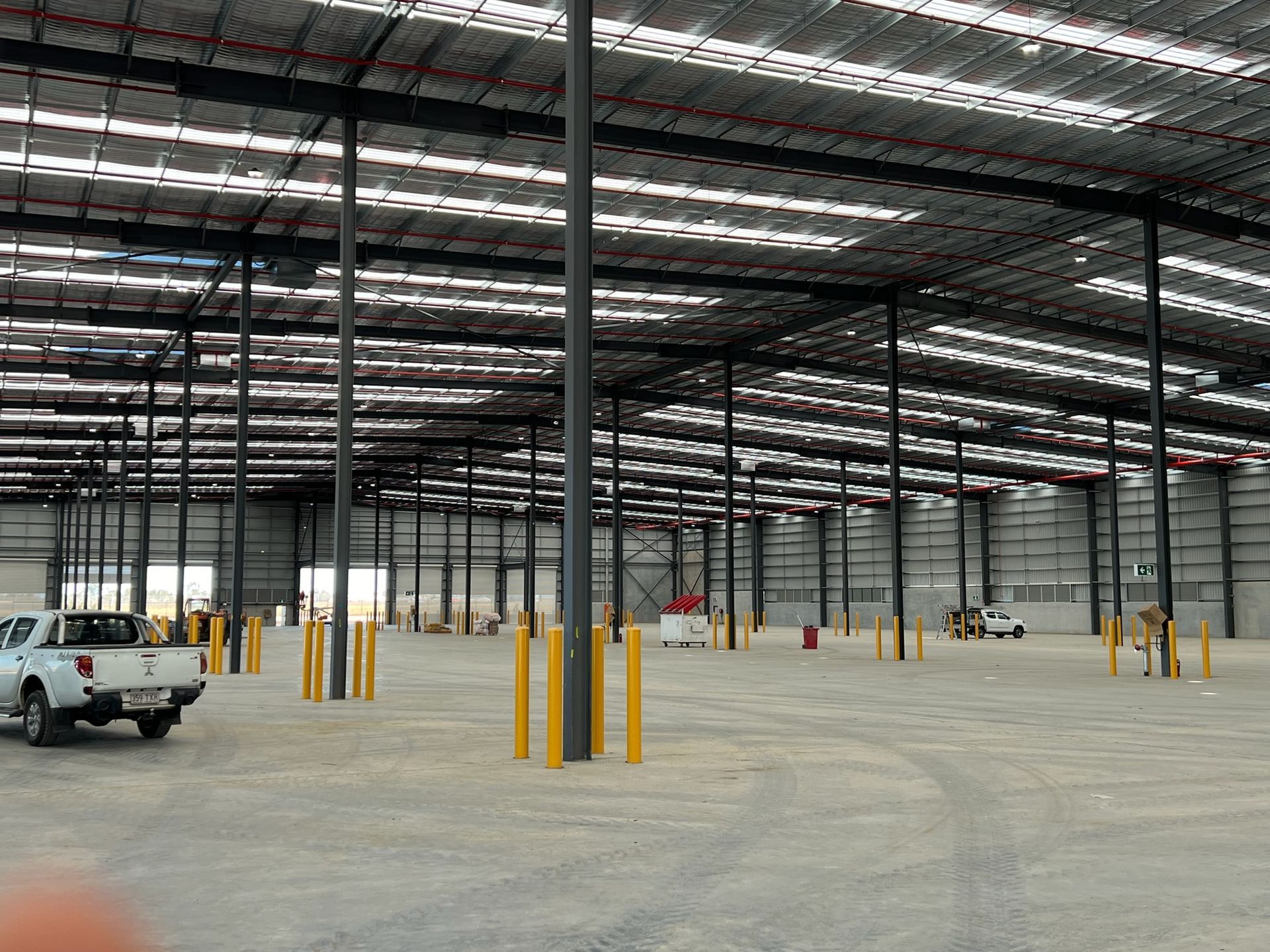 Empty warehouse interior with steel columns, overhead lights, and a white pickup truck near the left side.
