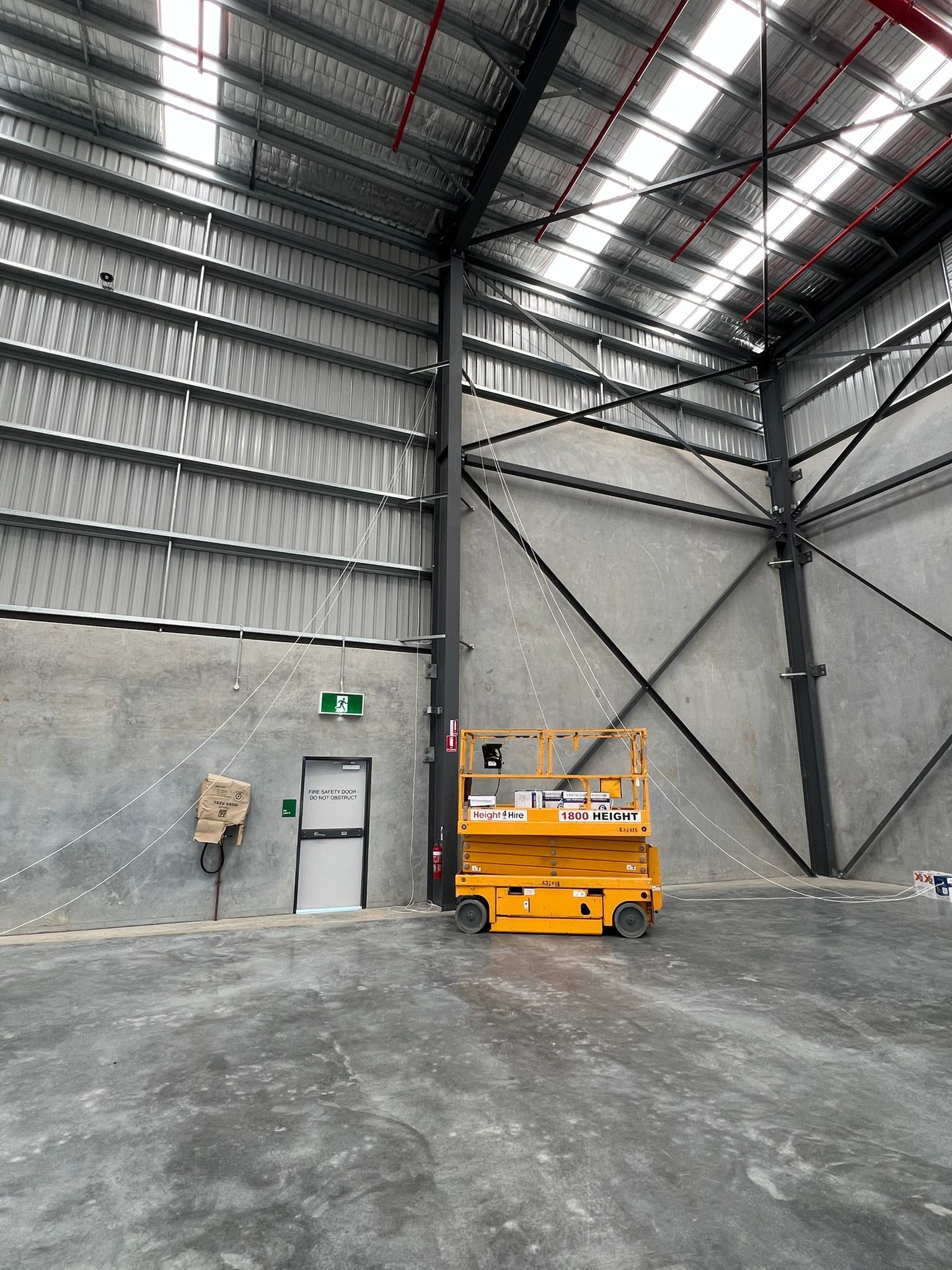 Large industrial warehouse interior with a yellow scissor lift, metal walls, and a concrete floor