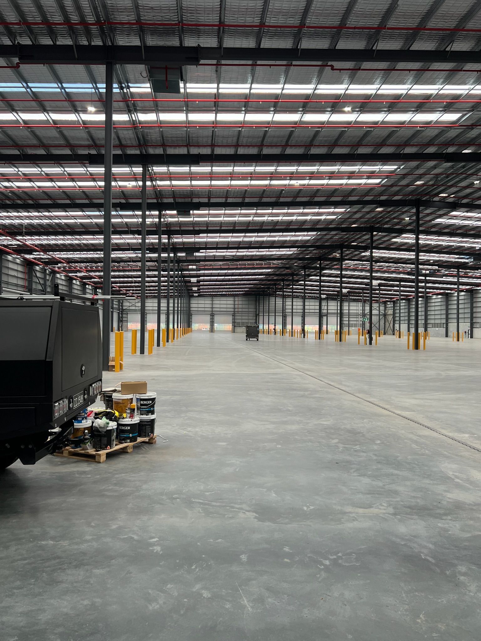 Empty warehouse interior with steel columns, overhead lights, and concrete floor.