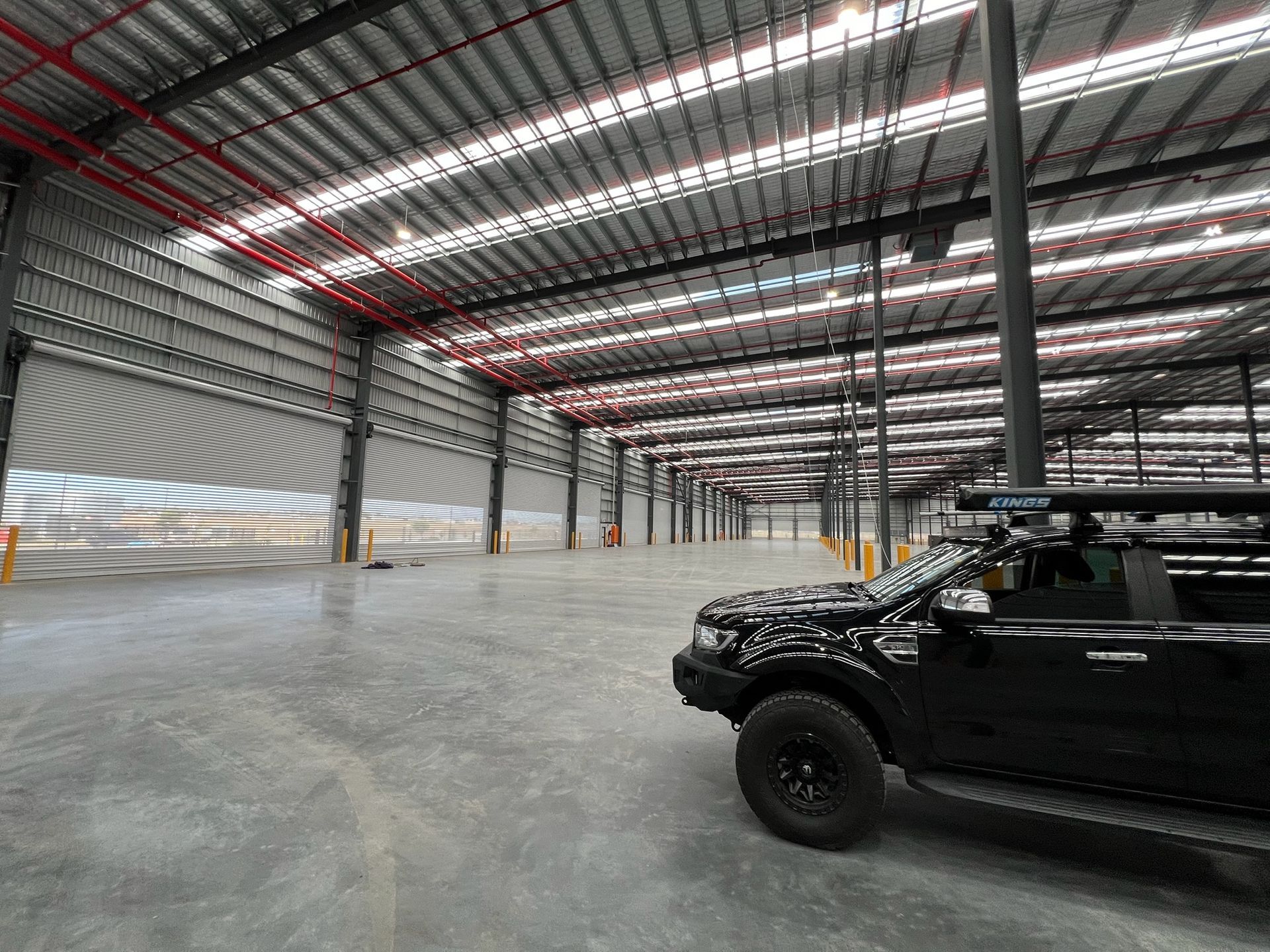 Empty industrial warehouse with a black off-road truck parked on the right side and skylit metal roofing above