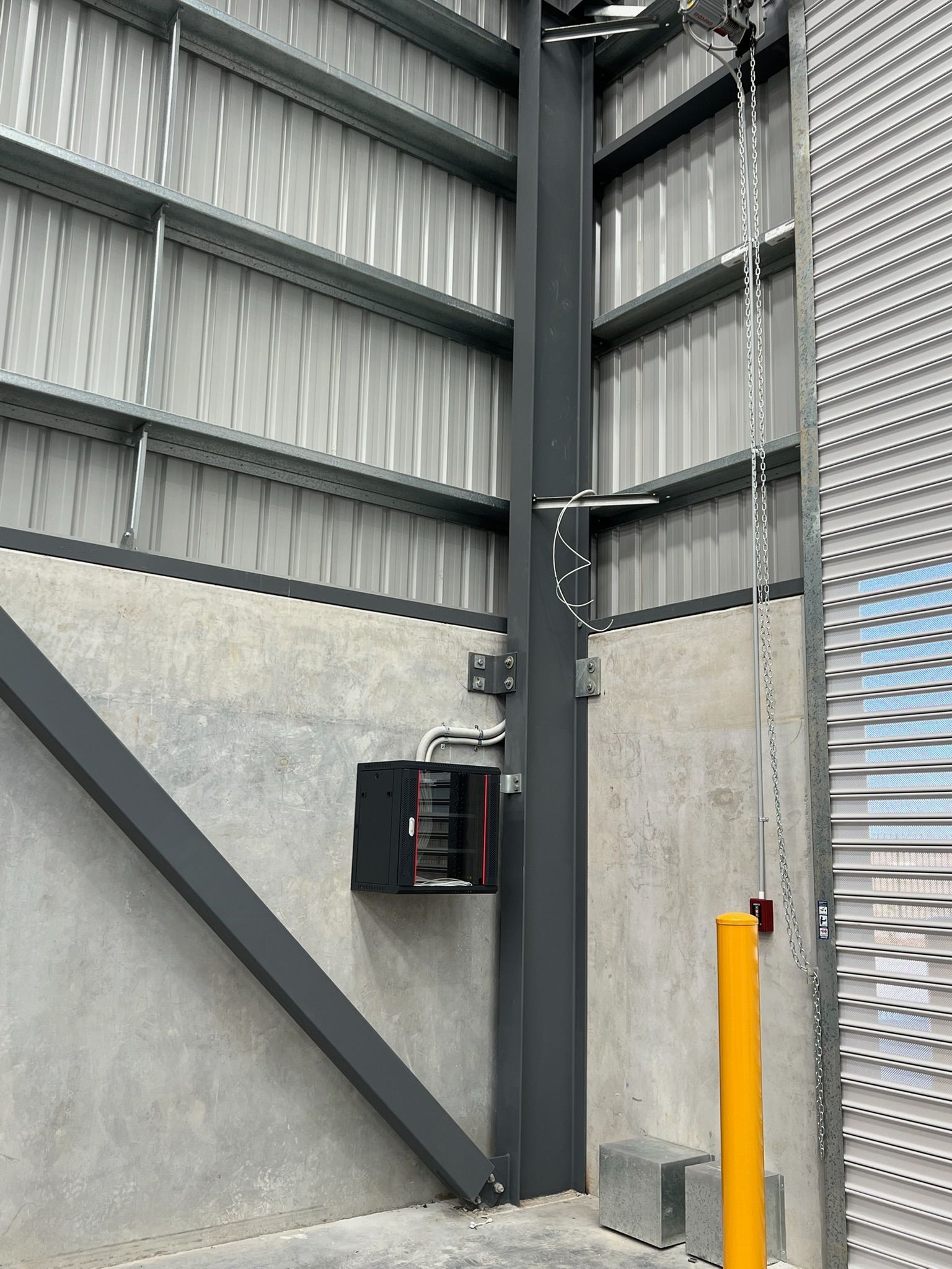 Industrial interior with gray metal wall panels, a black column, and an orange bollard near a control box