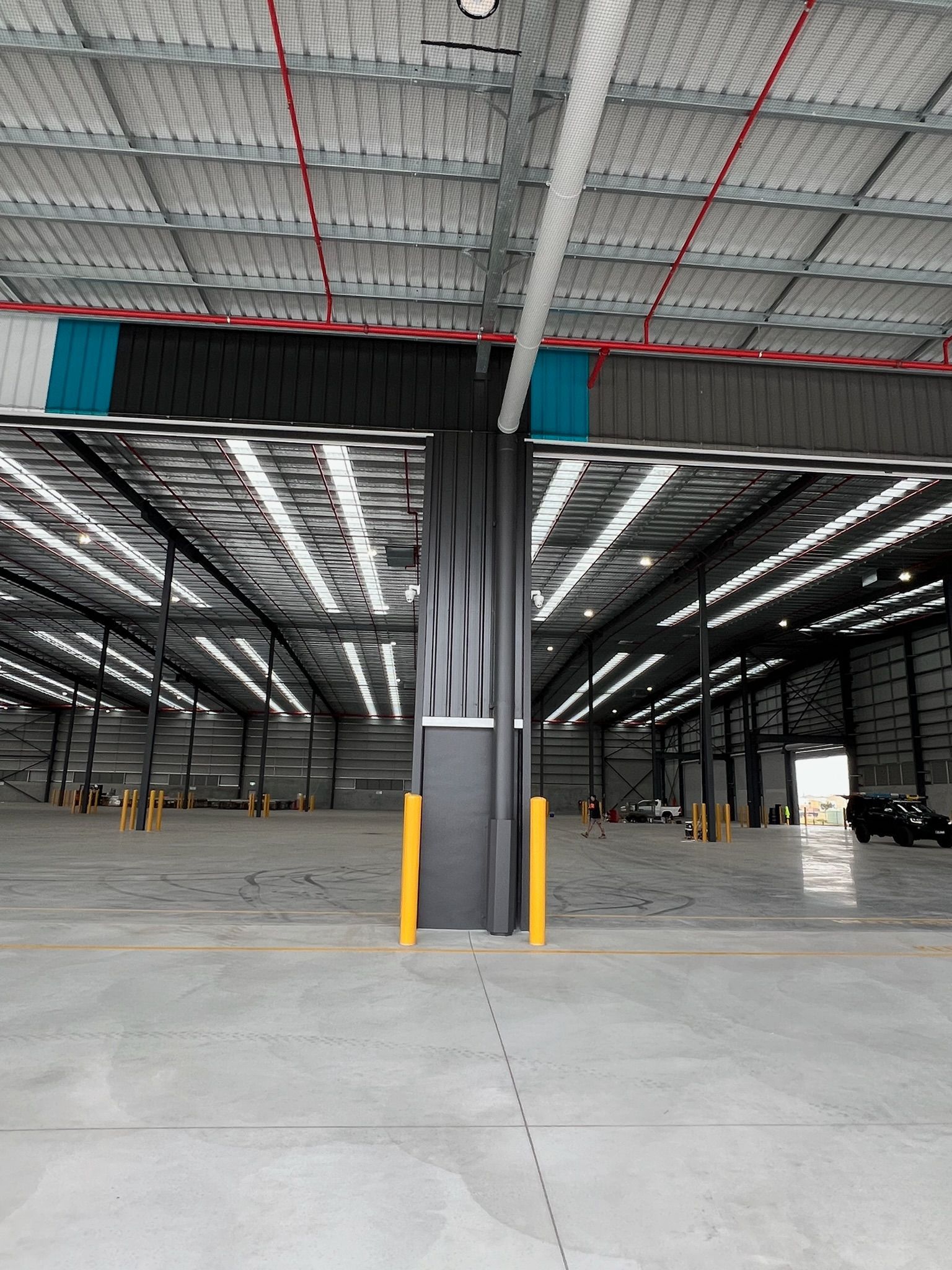 Empty warehouse interior with a central support column and concrete floor under a high metal roof